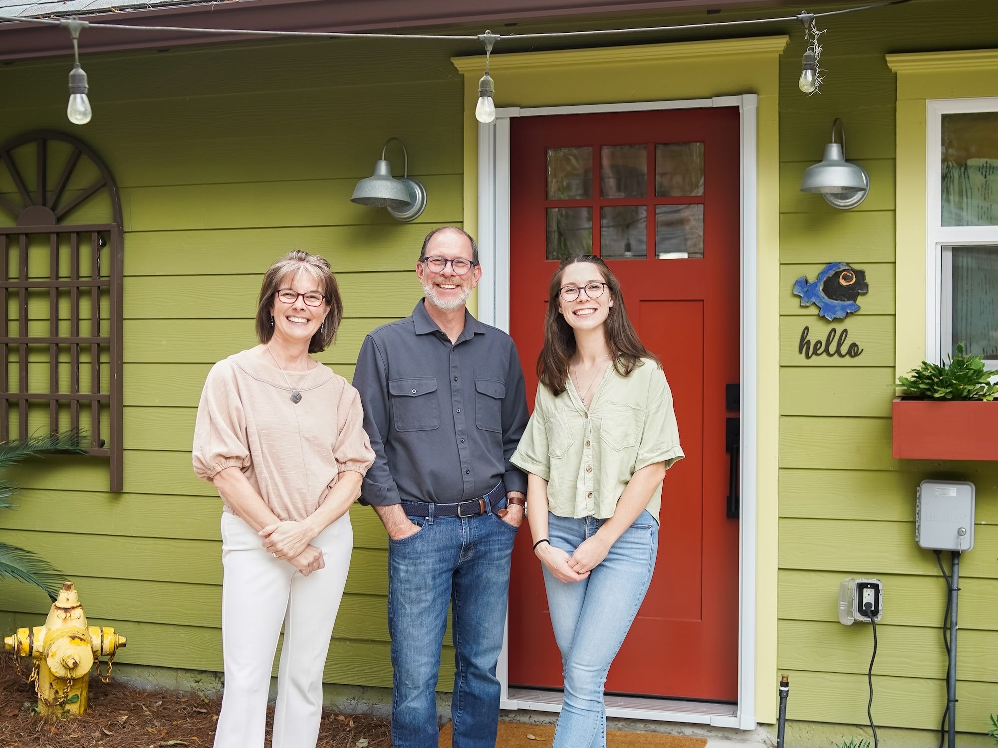 A photo of three people in front of a green apartment with a red door.