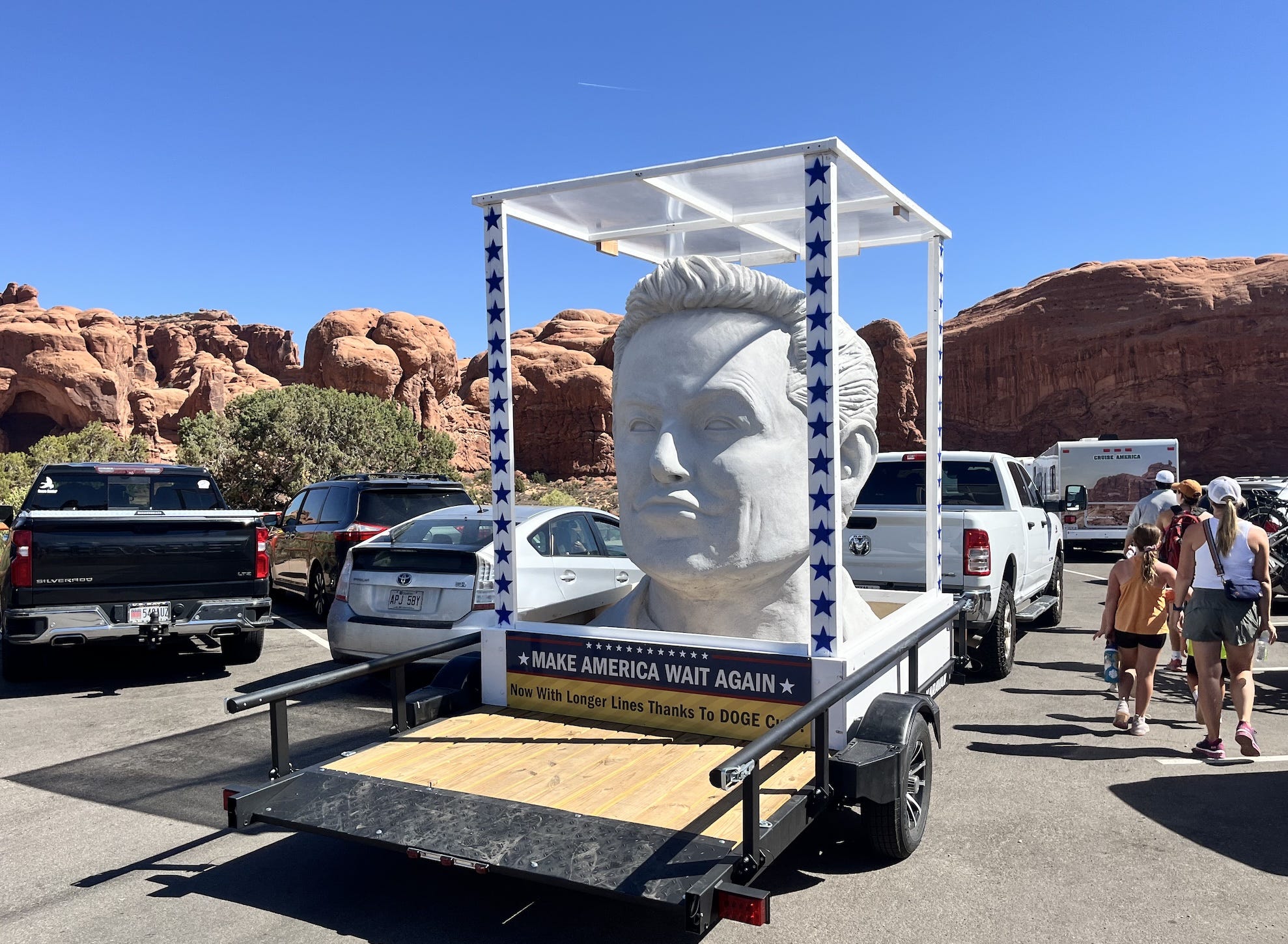 A large bust of Elon Musk on a trailer behind a pickup truck.