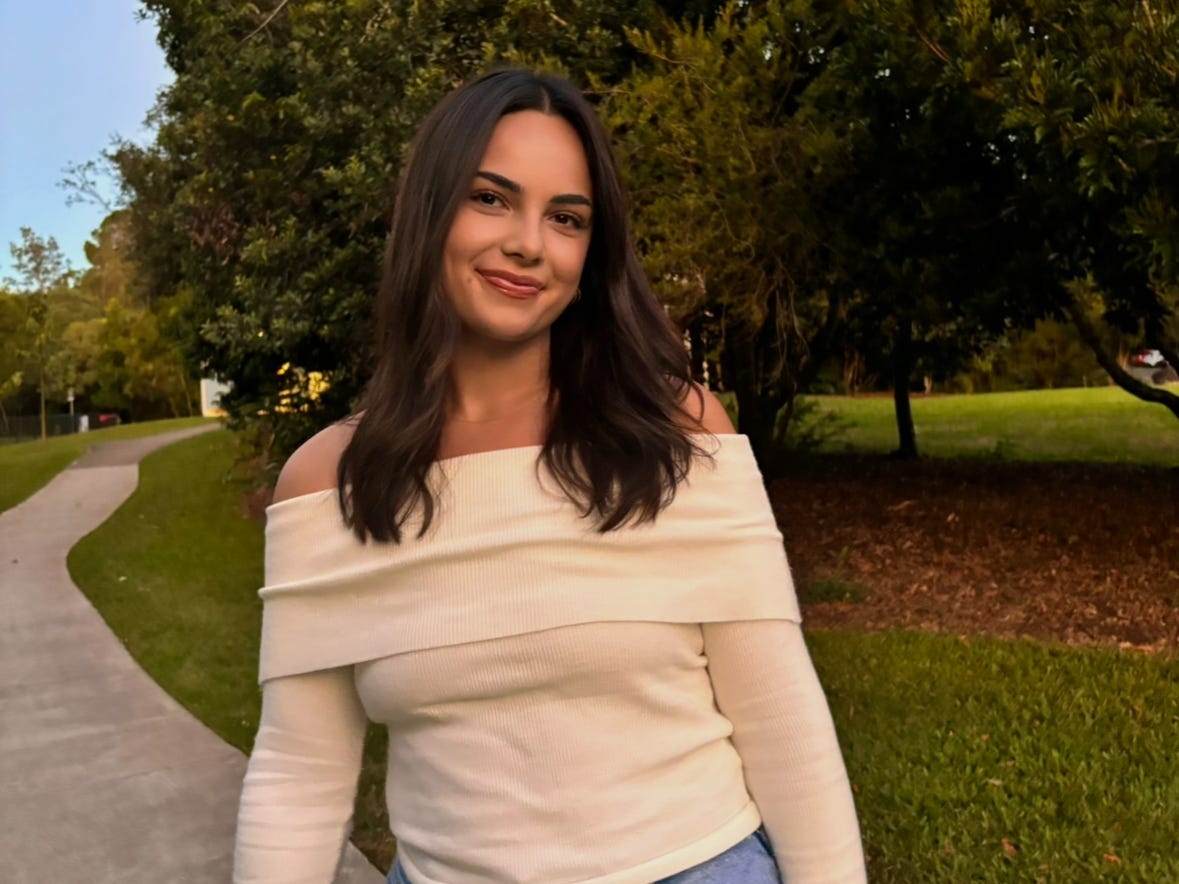 A woman wearing a cream sweater and jeans, smiling outside.