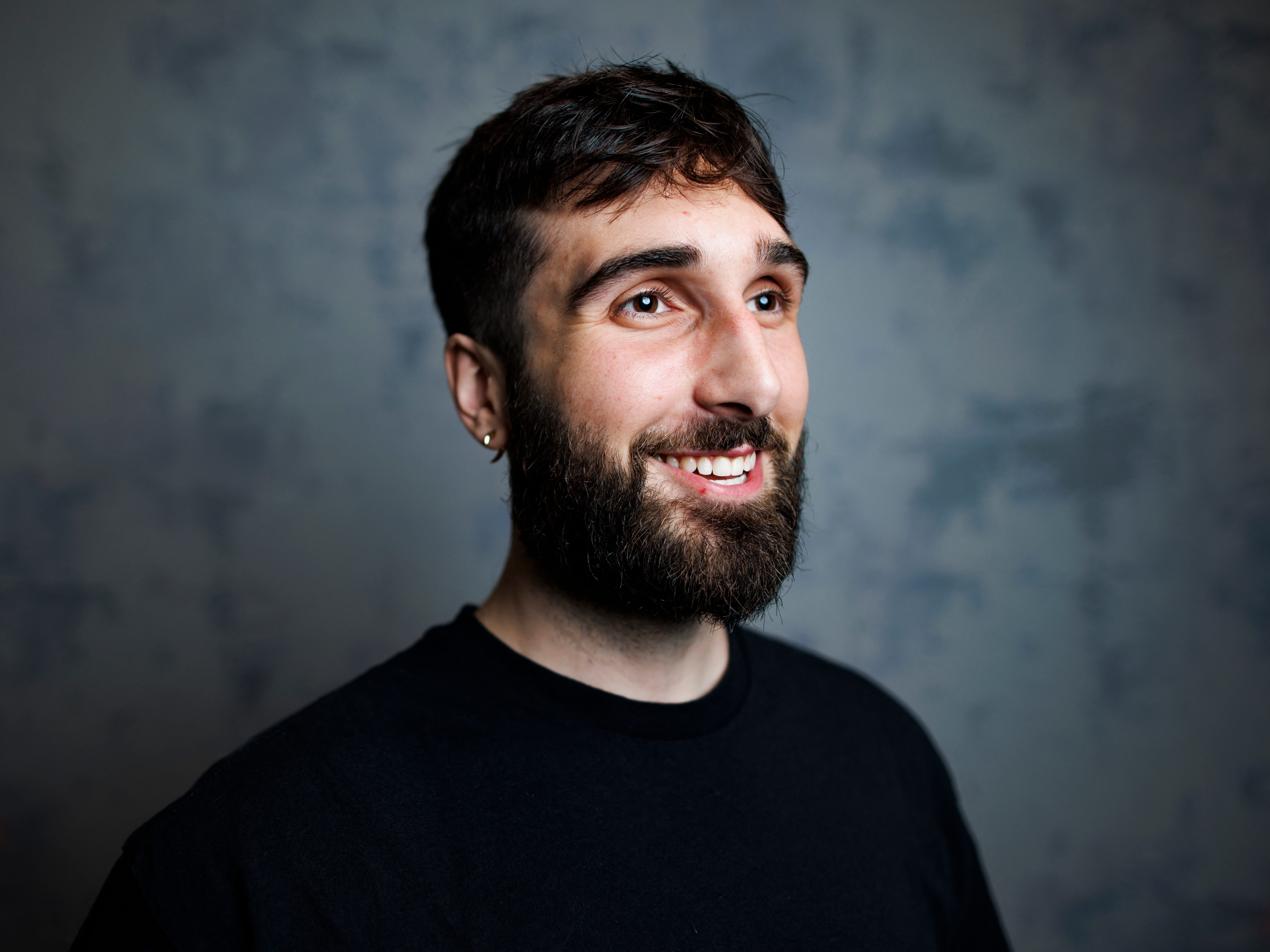 A white bearded man smiles against a photo studio backdrop.
