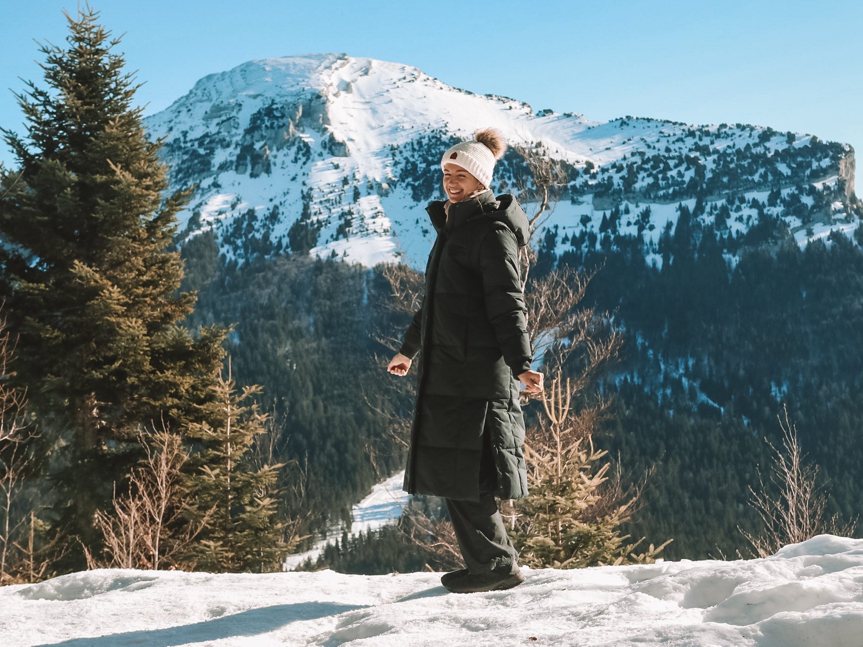 The author in Grenoble, France, wearing a puffer jacket and standing in the snow with a mountain in the background.