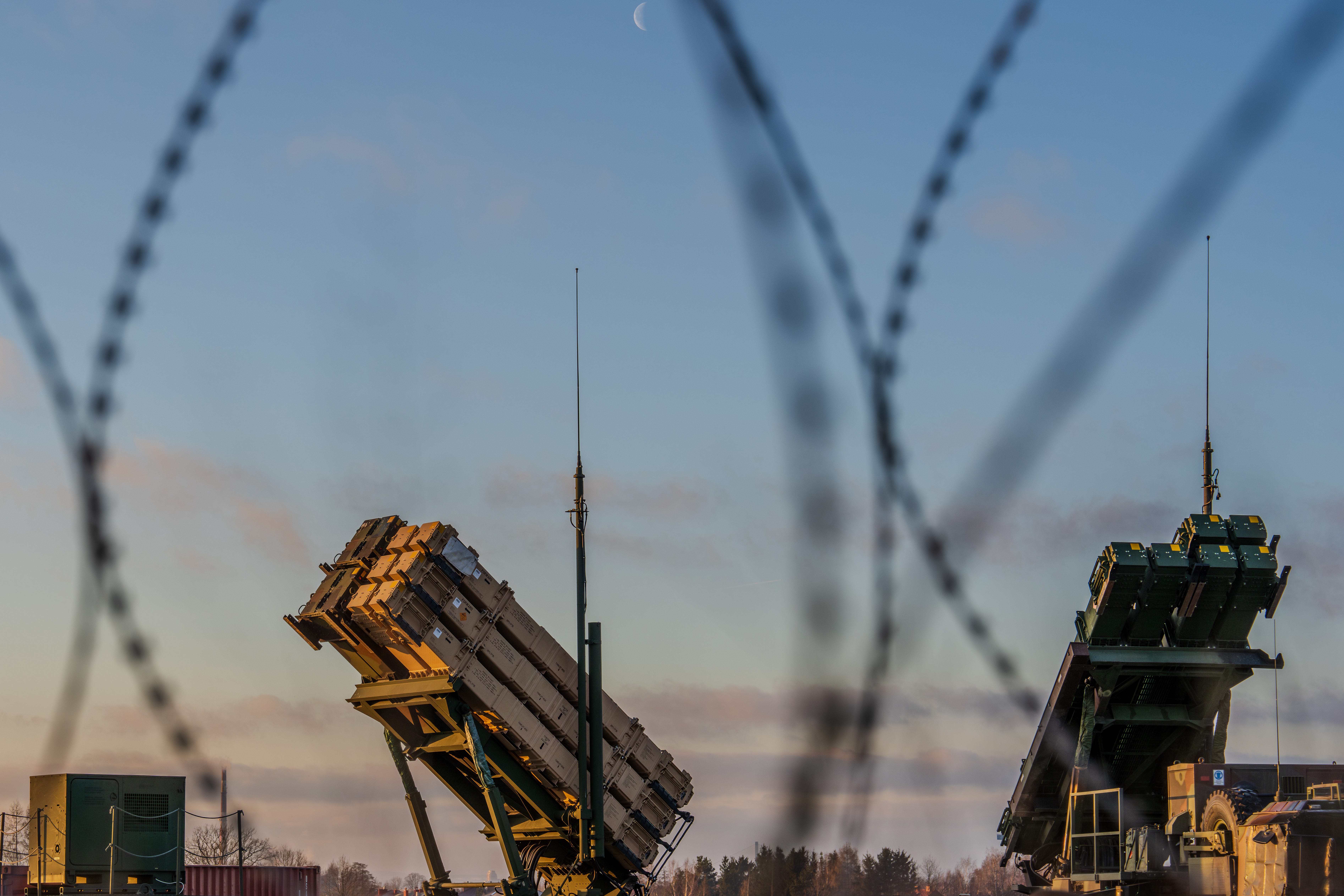 A Patriot missile launcher is erected at an airfield in eastern Poland, seen through blurred out barbed wire.