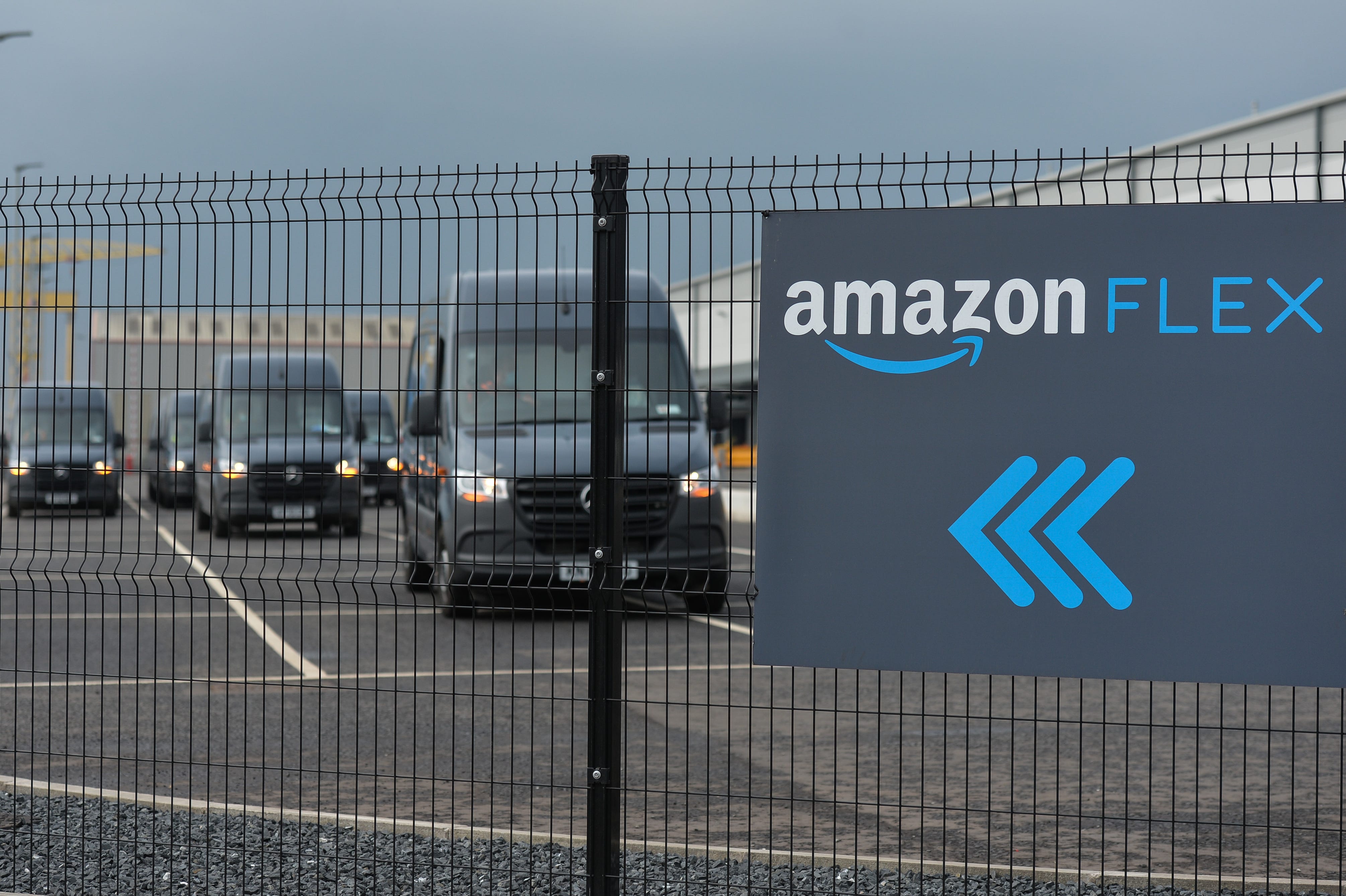 An Amazon Flex sign is shown with delivery vehicles behind a fence