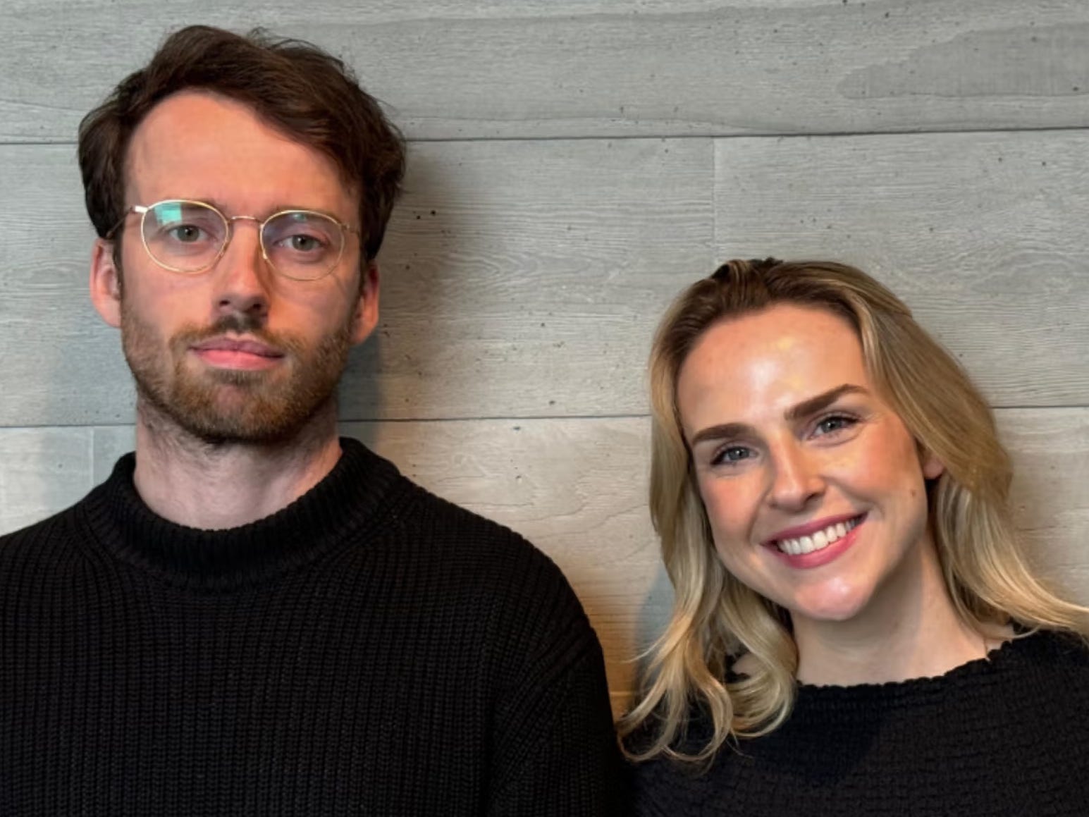 Anam cofounders Ben Carr and Caoimhe Murphy, both wearing black sweaters in front of a wooden wall.