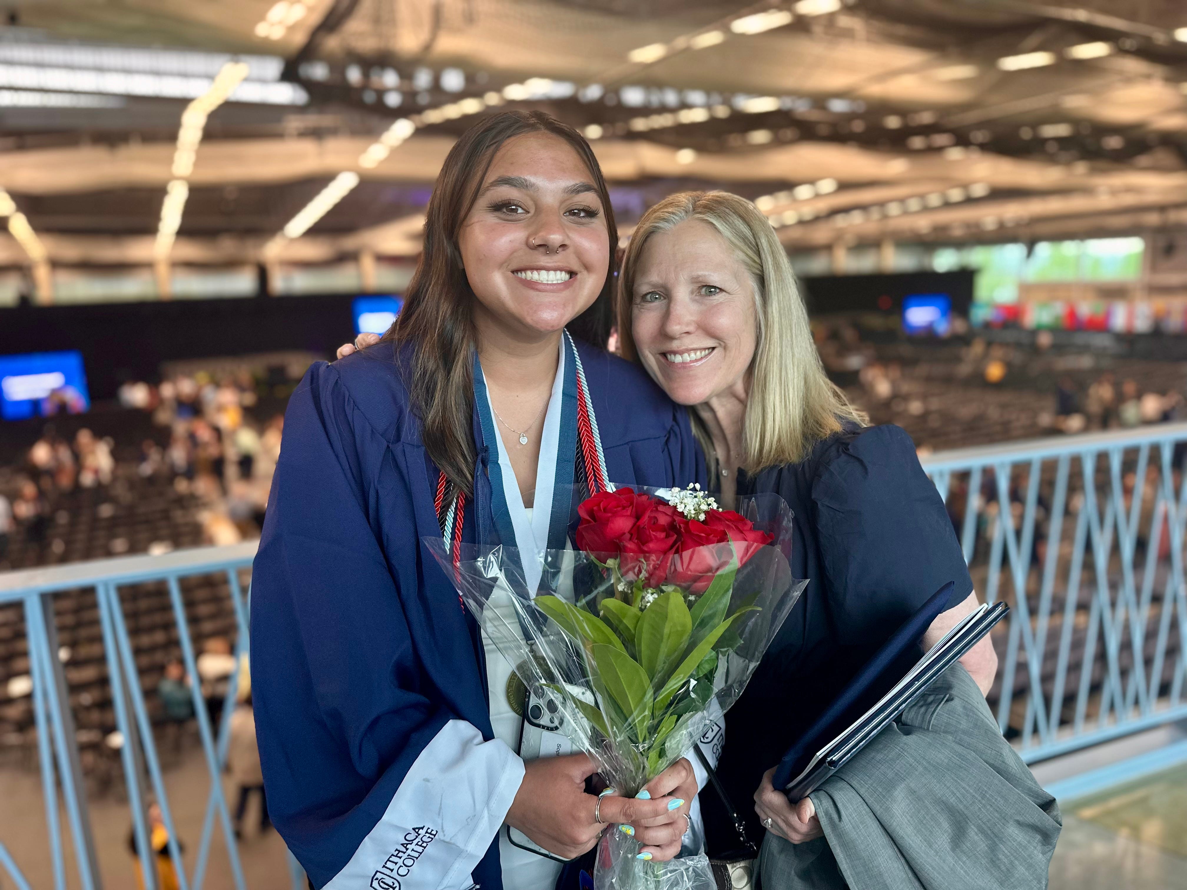 A woman stands with a recent college graduate who is holding red roses.