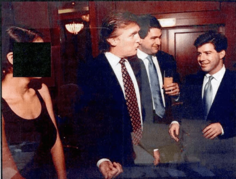 A woman with a black bar over her face, Donald Trump and two other men in a wood-lined room.