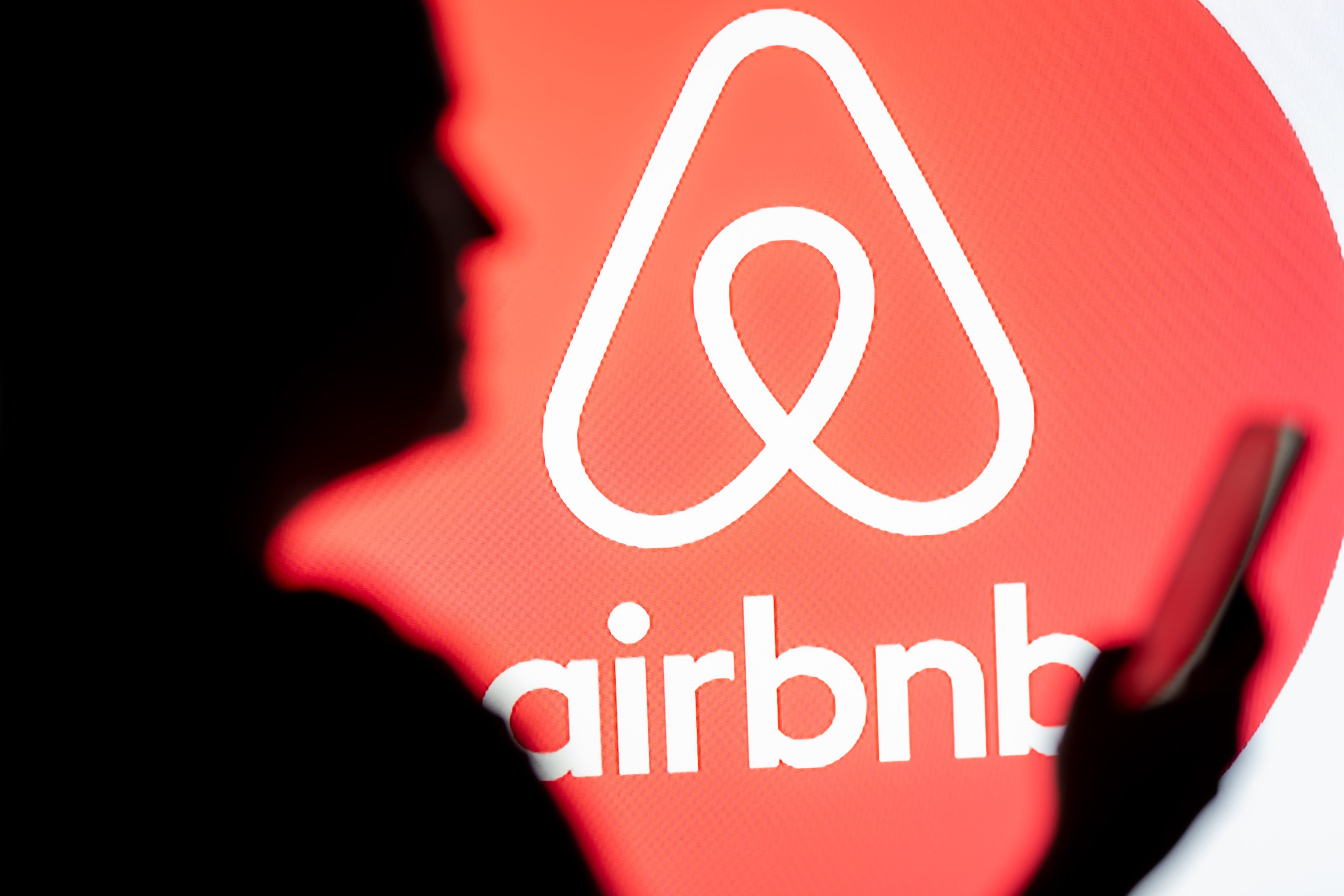 A silhouette of someone using a phone in front of an Airbnb logo