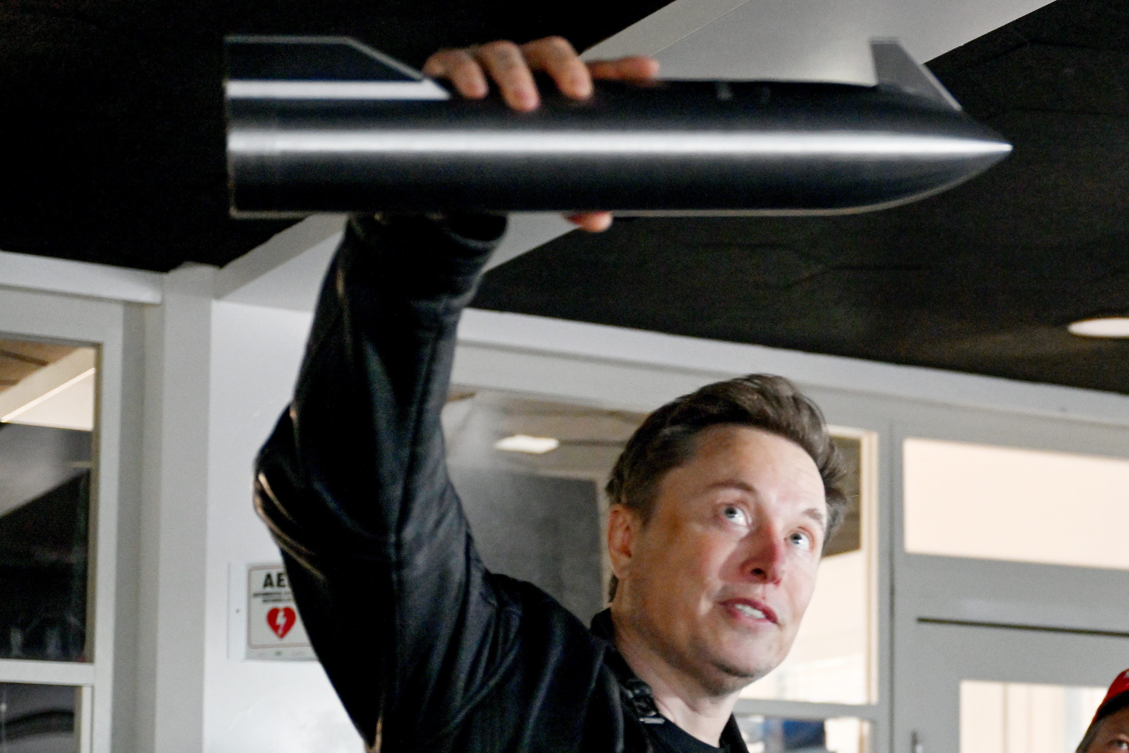 Elon Musk holding a model of a rocket and explaining it to President Donald Trump and other visitors.