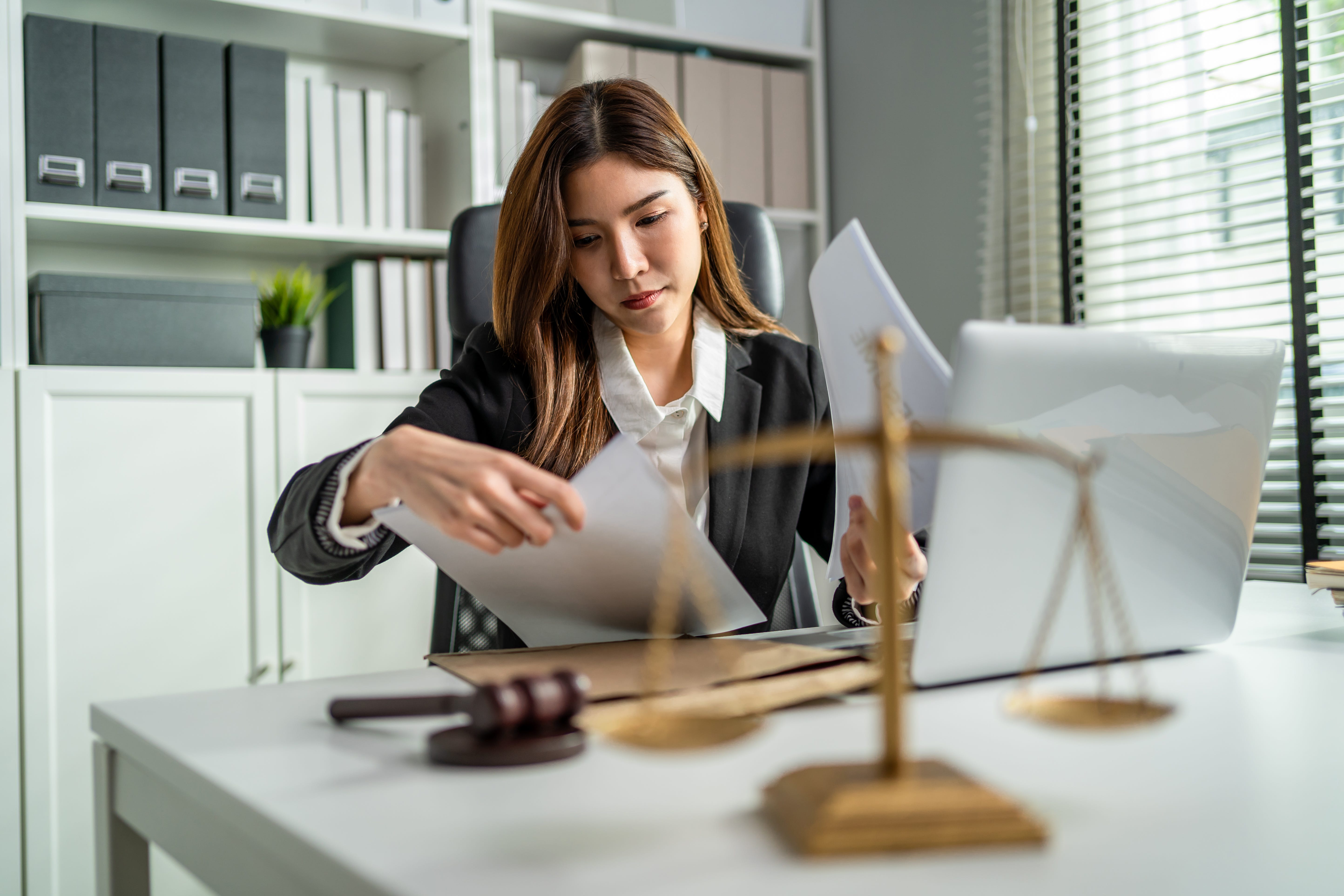 A woman in a suit, with the scales of justice on her desk.