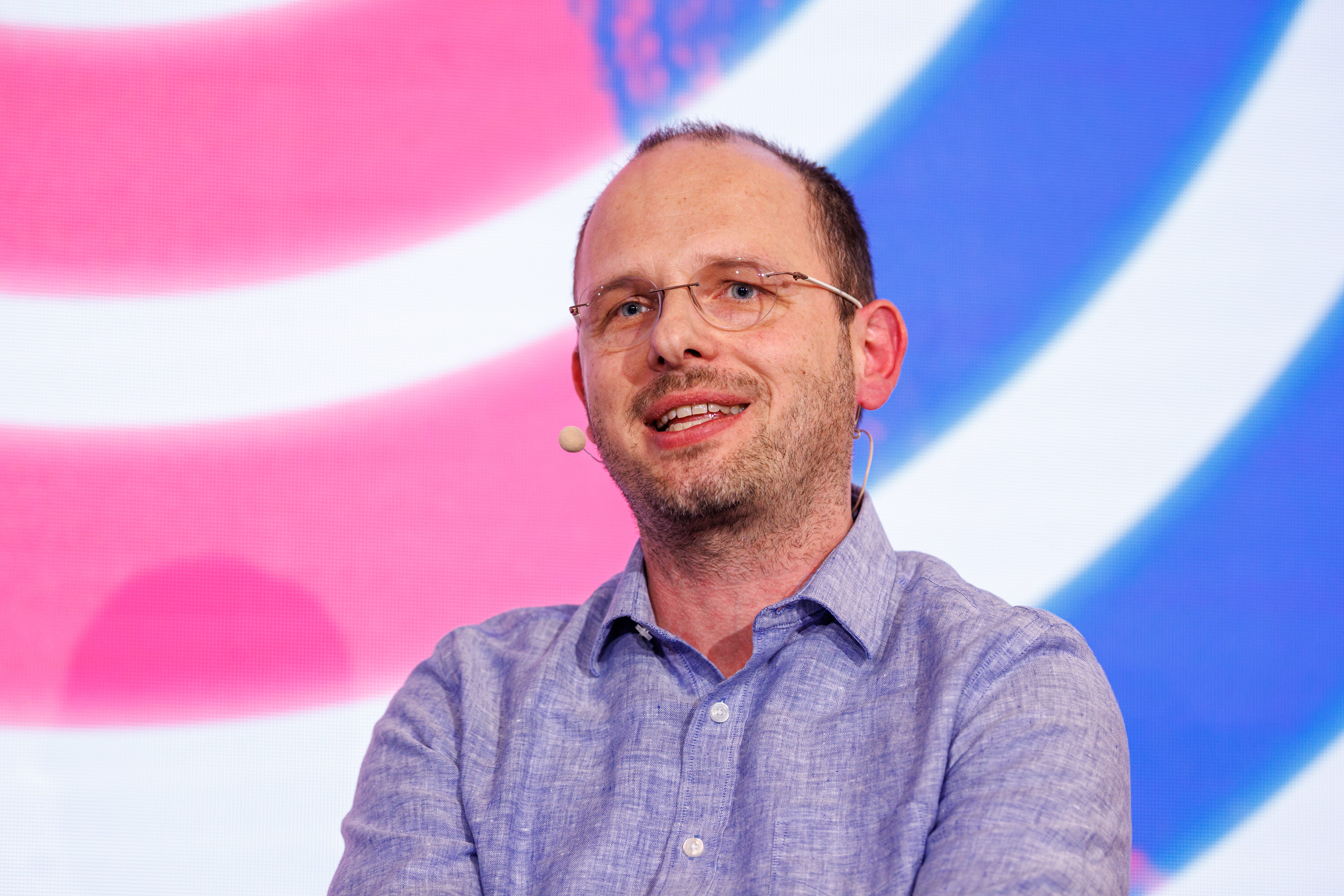 Thomas Dohmke, CEO of Github, speaks at the Digital Life Design (DLD) innovation conference. DLD is a conference on internet trends and developments in digitalization. He is wearing a mic and is mid speech.