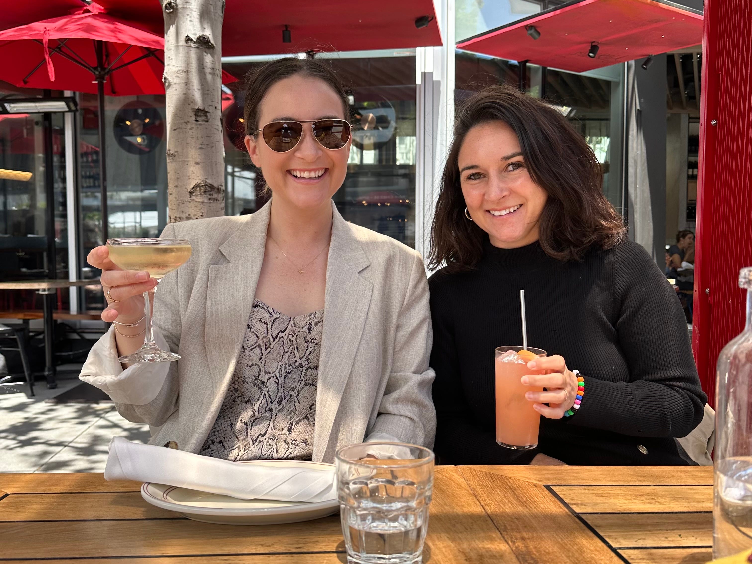 The author and her sister sitting at a table outside and holding up drinks while smiling.