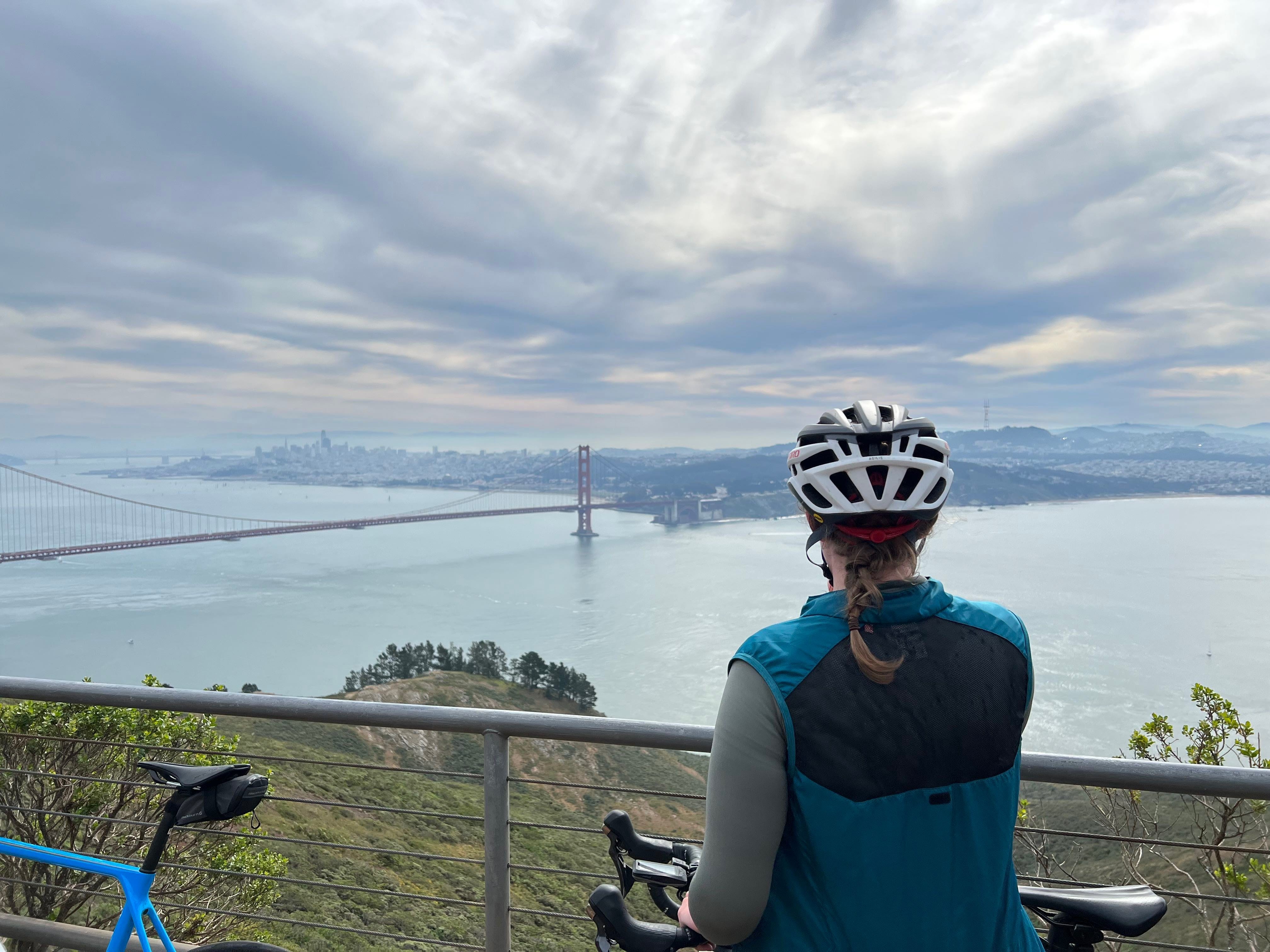 The author's back is to the camera as she looks out to the Golden Gate Bridge. She's wearing biking gear.
