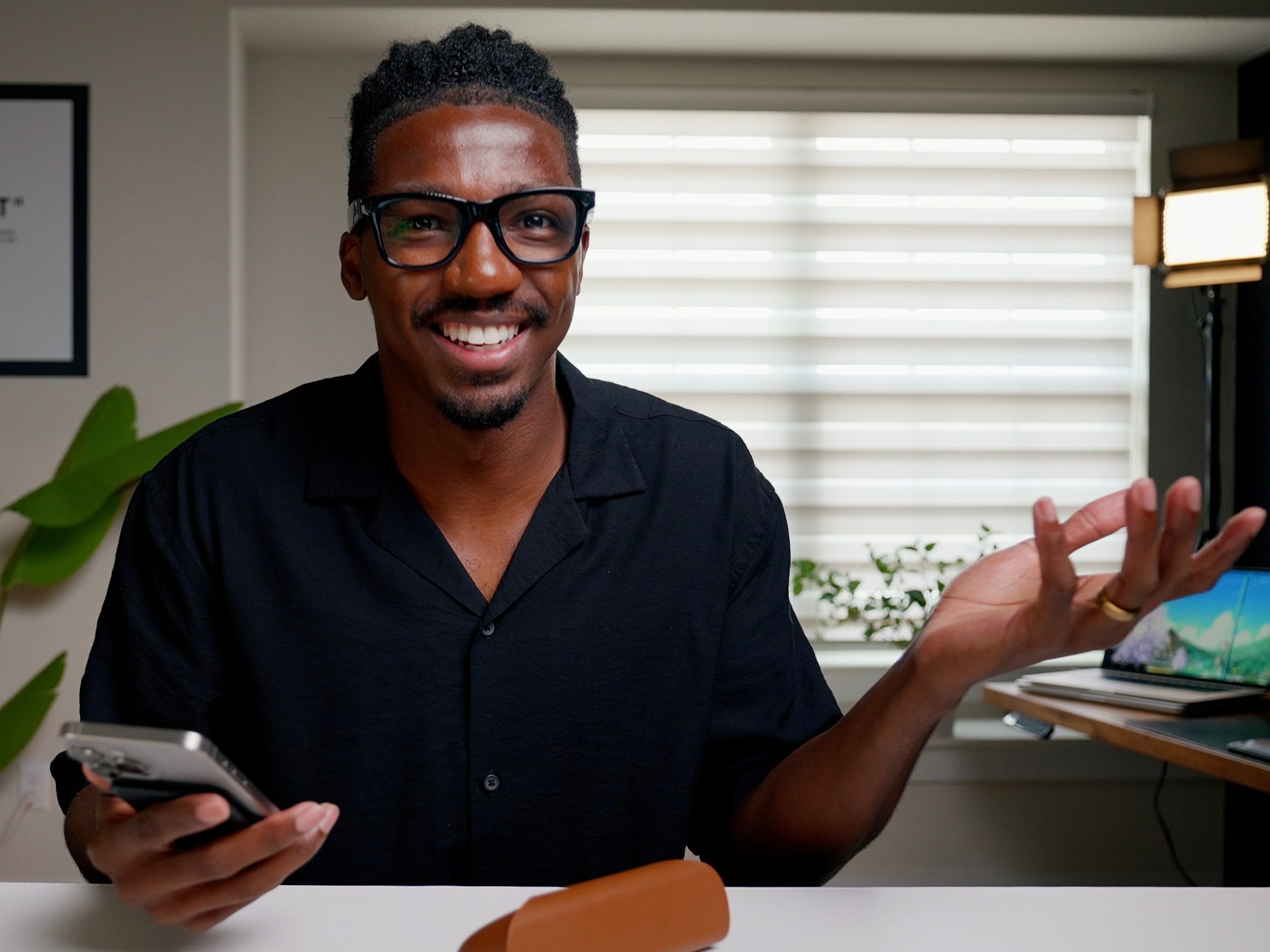 Jeremiah Peoples is smiling and holding a phone at his desk