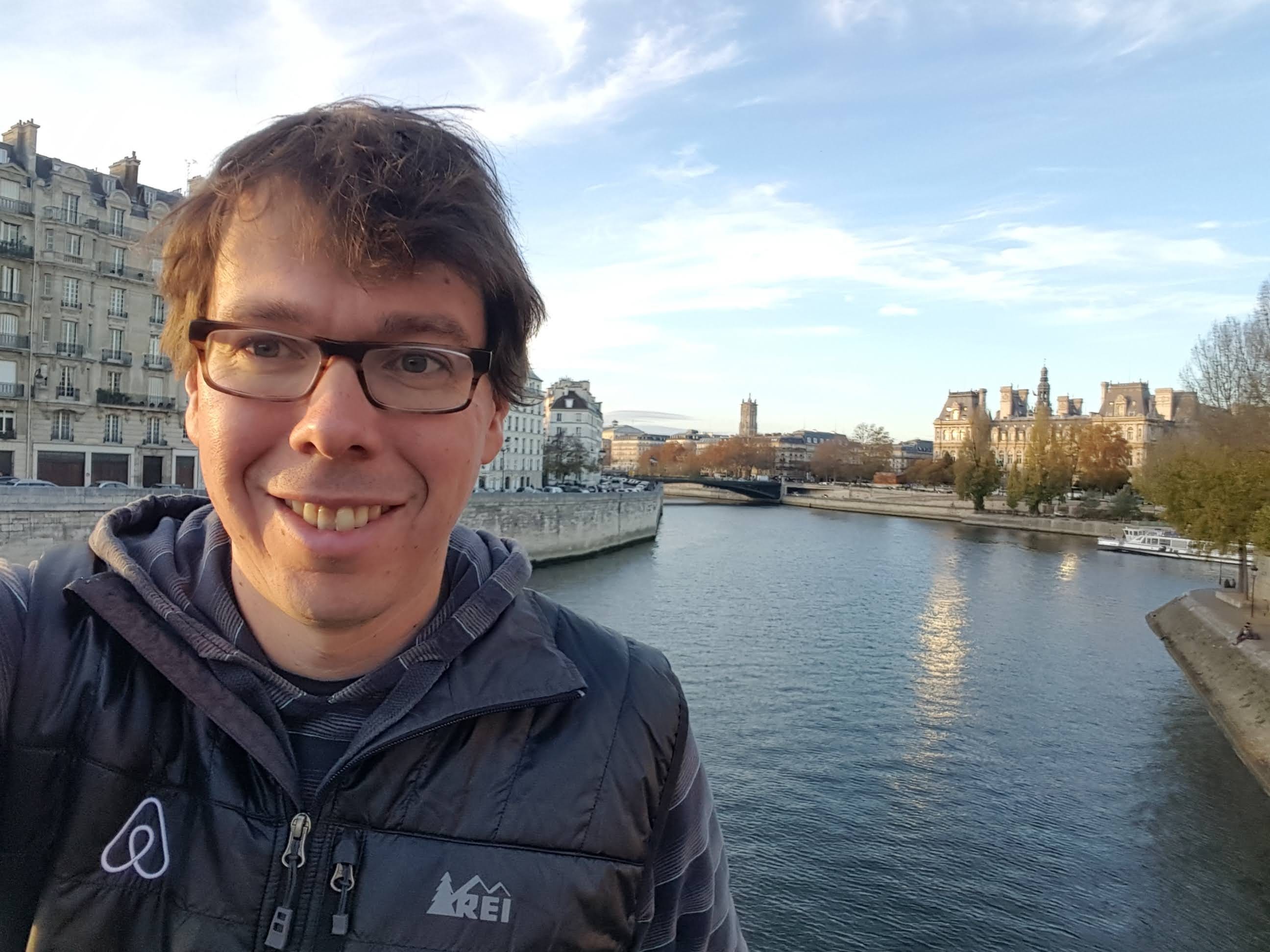 Judd Antin standing in front of a river. He's wearing a coat with the Airbnb logo.