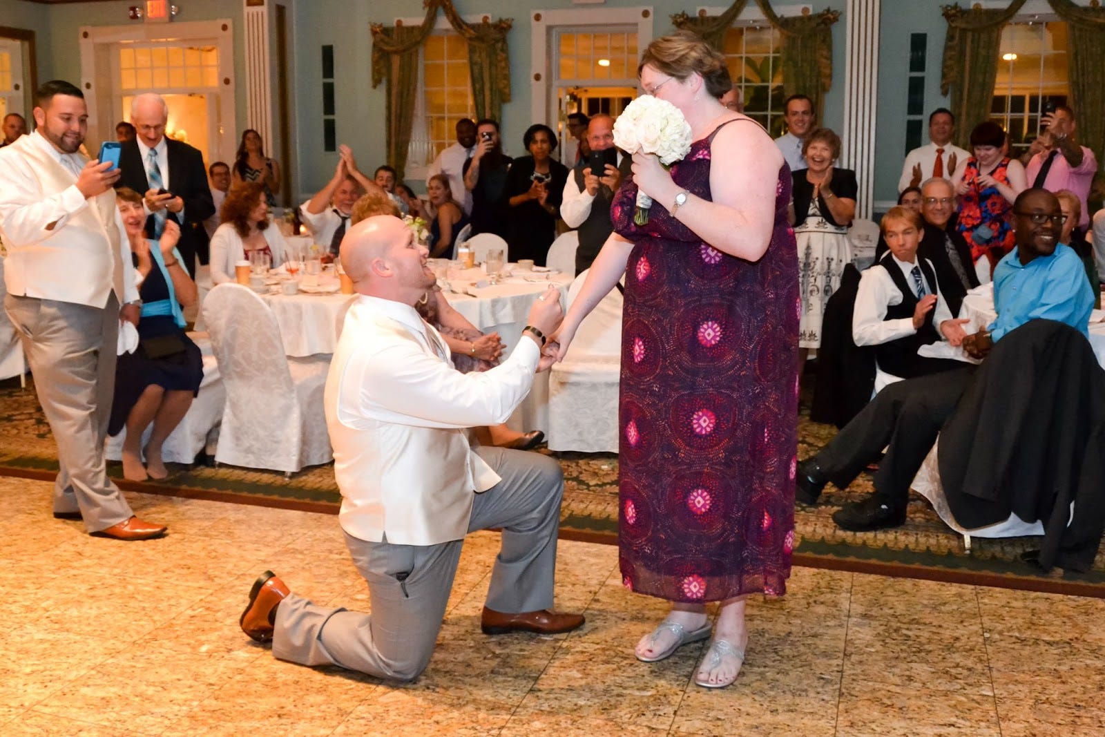 Man proposing to a woman who's holding a bouqet at wedding