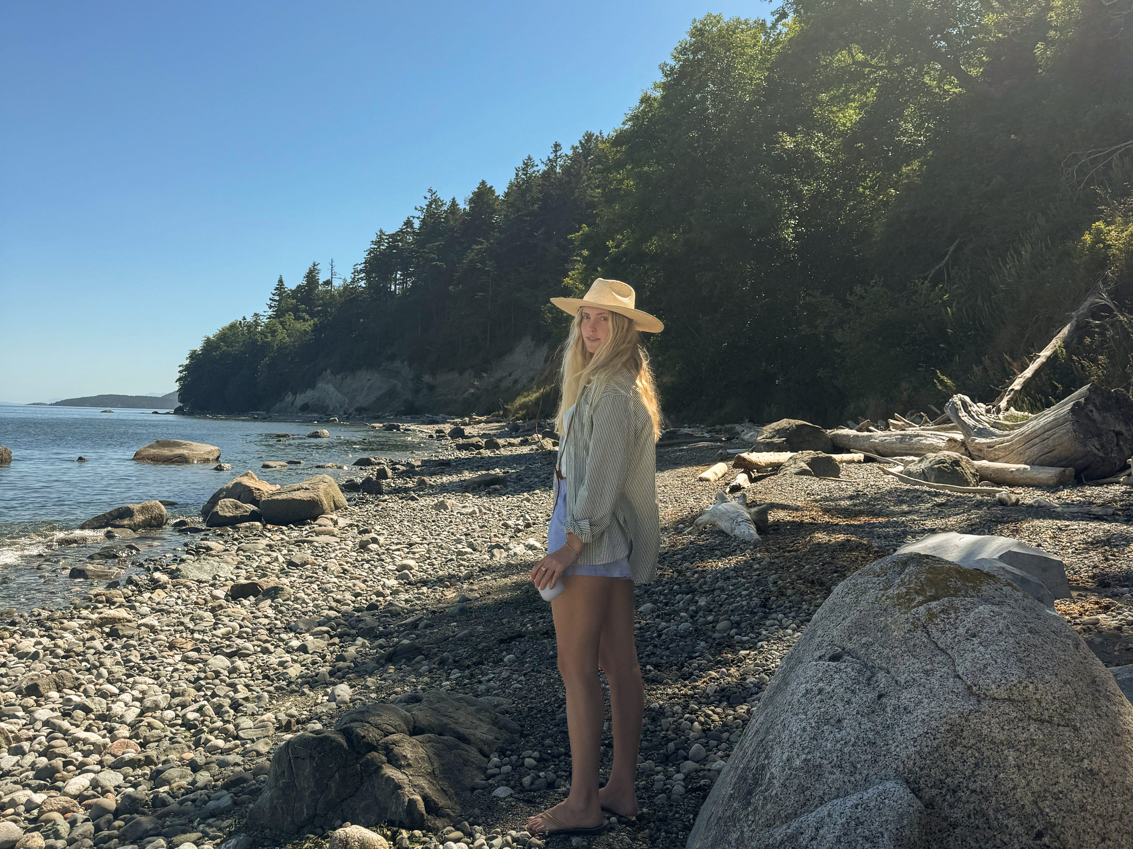 Blakely stands on a rocky beach with trees behind her.
