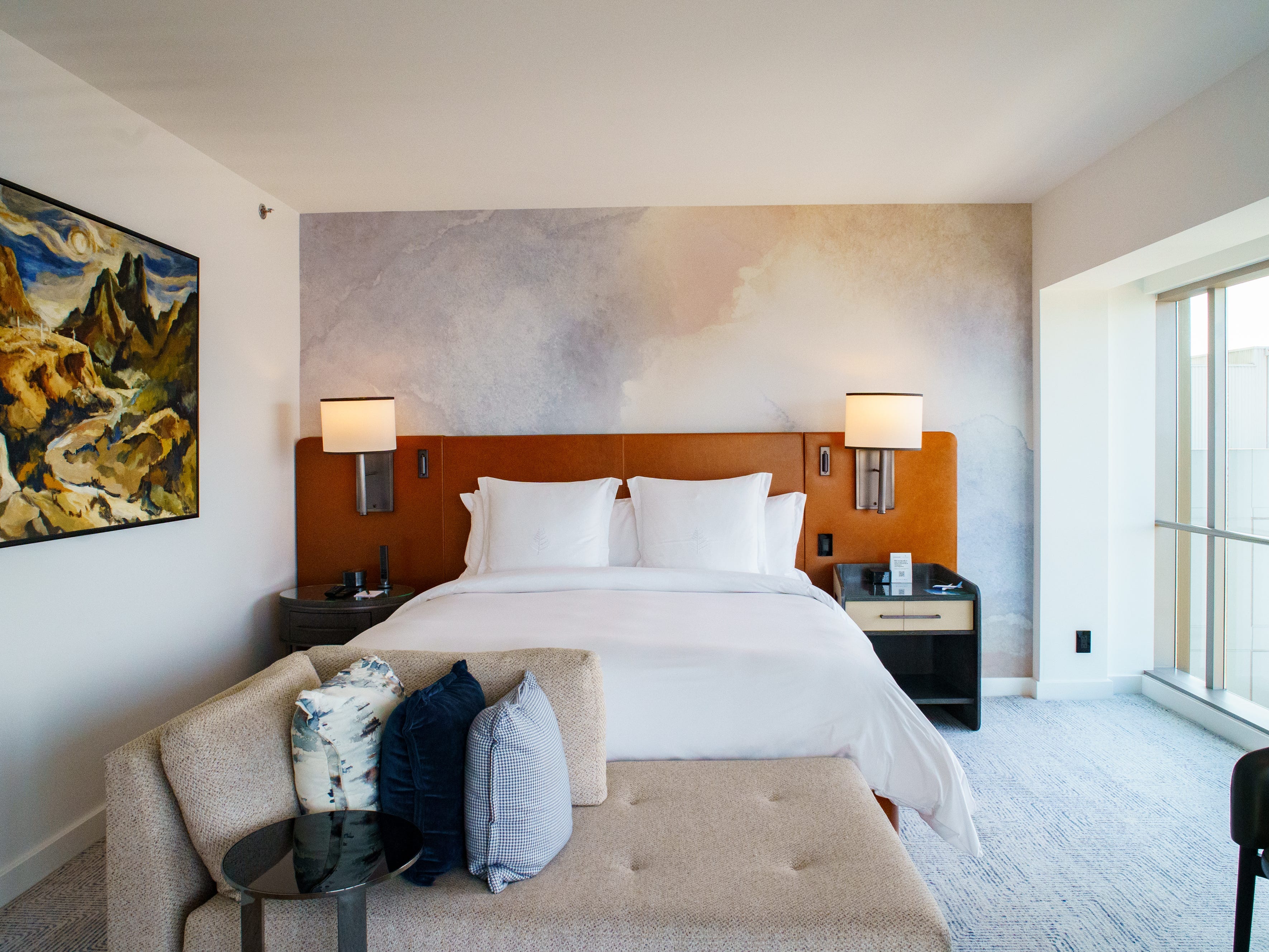 Inside a Four Seasons Seattle hotel room with a painting on the left, a bed in the middle, and windows on the right