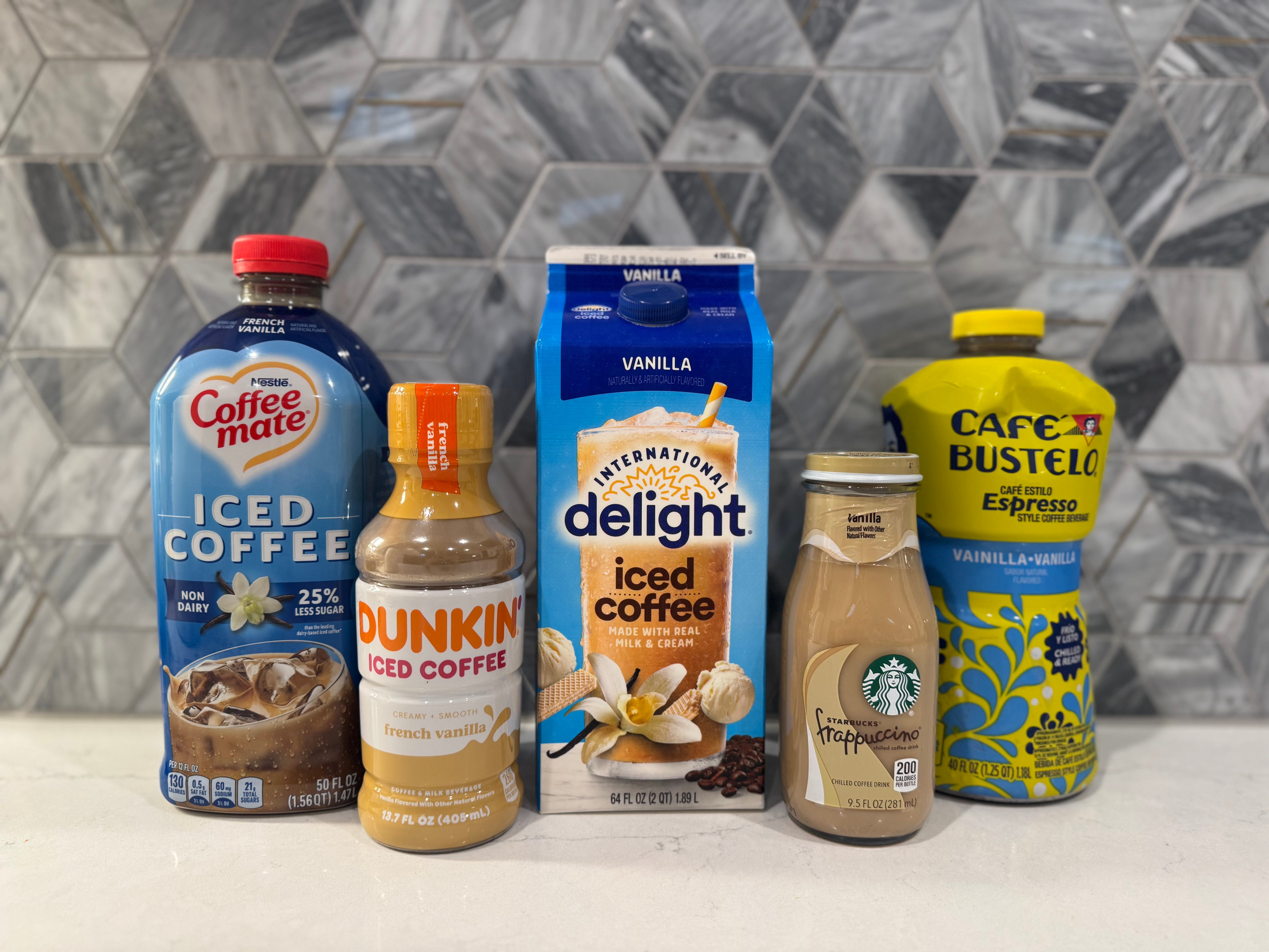 Vanilla iced CoffeeMate, Dunkin, International Delight, Starbucks, and Cafe Bustelo coffee bottles in front of gray backsplash