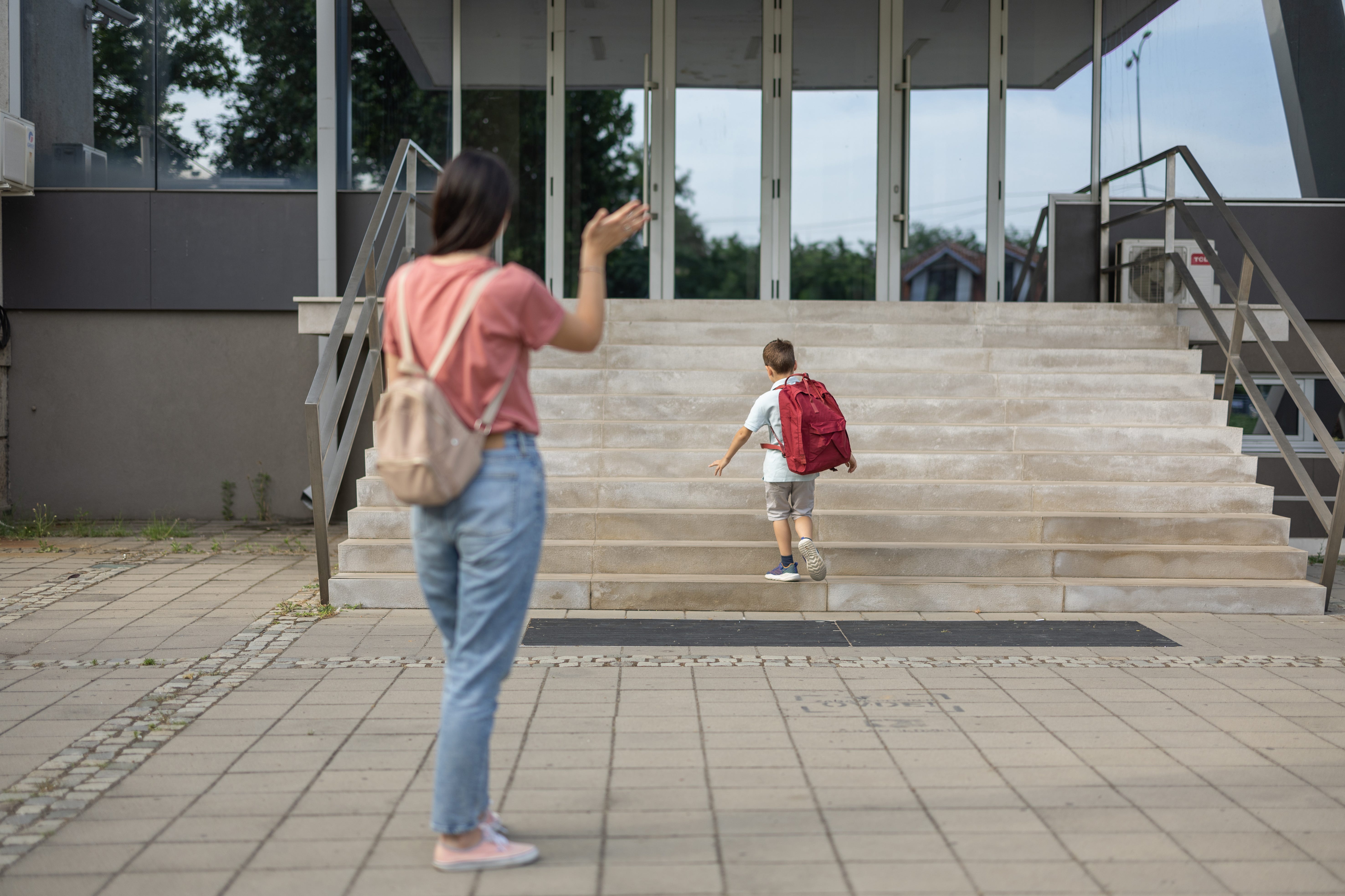 Mom waves goodbye to her son as he heads into school.