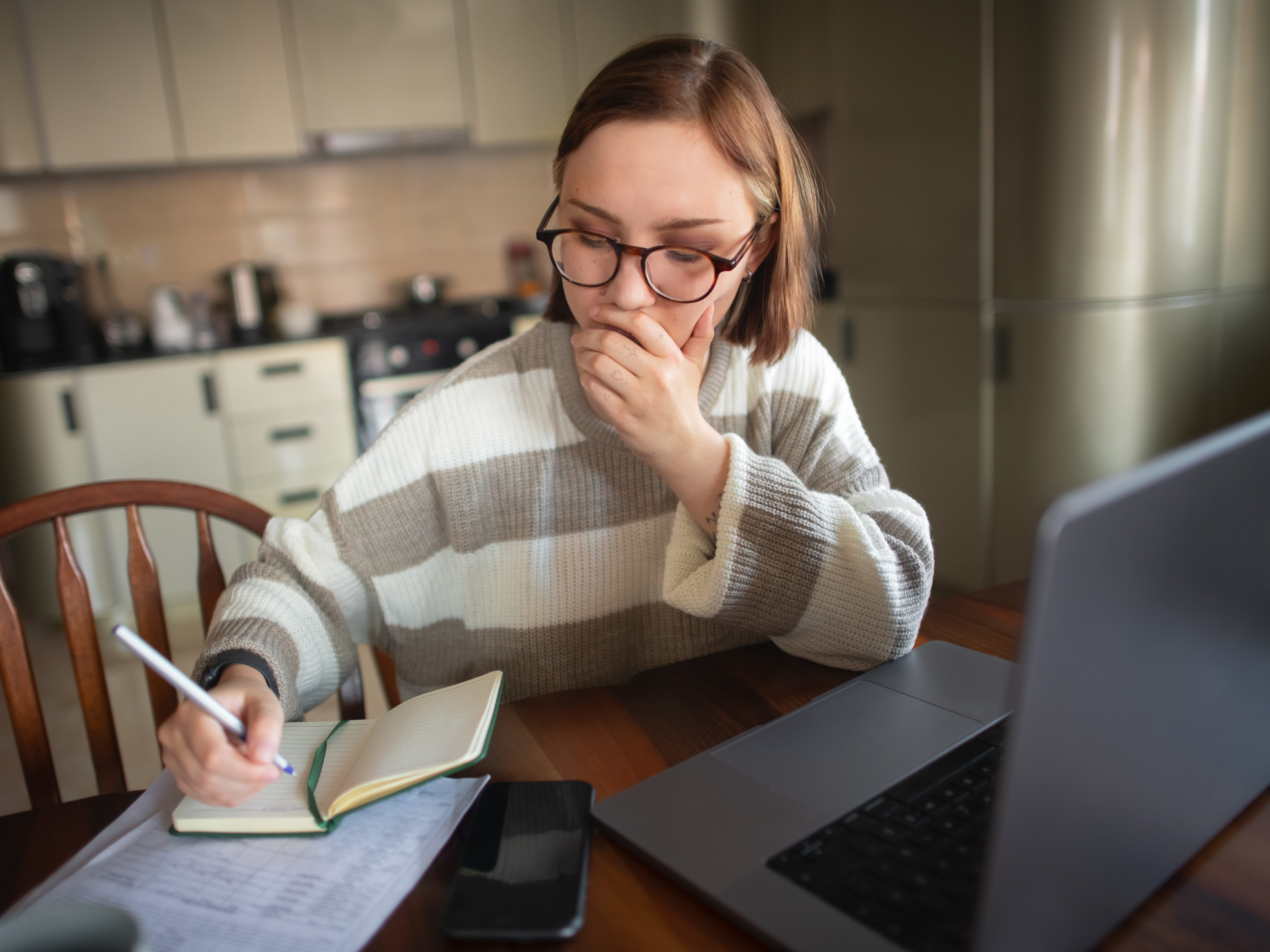 a woman sitting at her computer and writing in a notebook