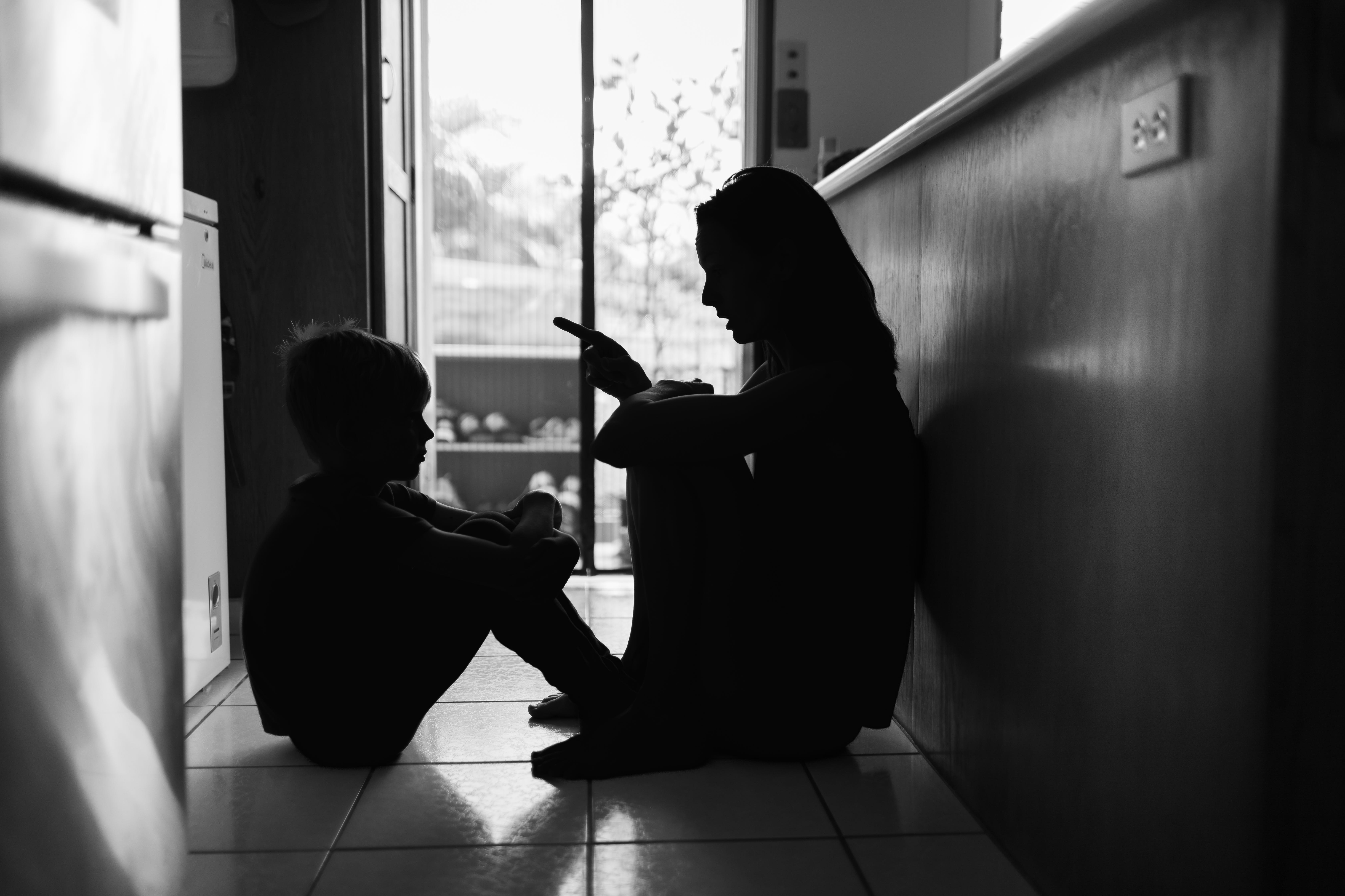 A son and mother sit in the floor and have a discussion.
