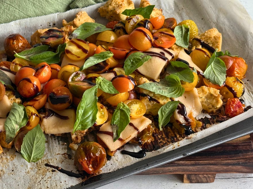 Tofu and tomatoes roasted on a sheet pan, drizzled with balsamic glaze, and garnished with basil leaves.