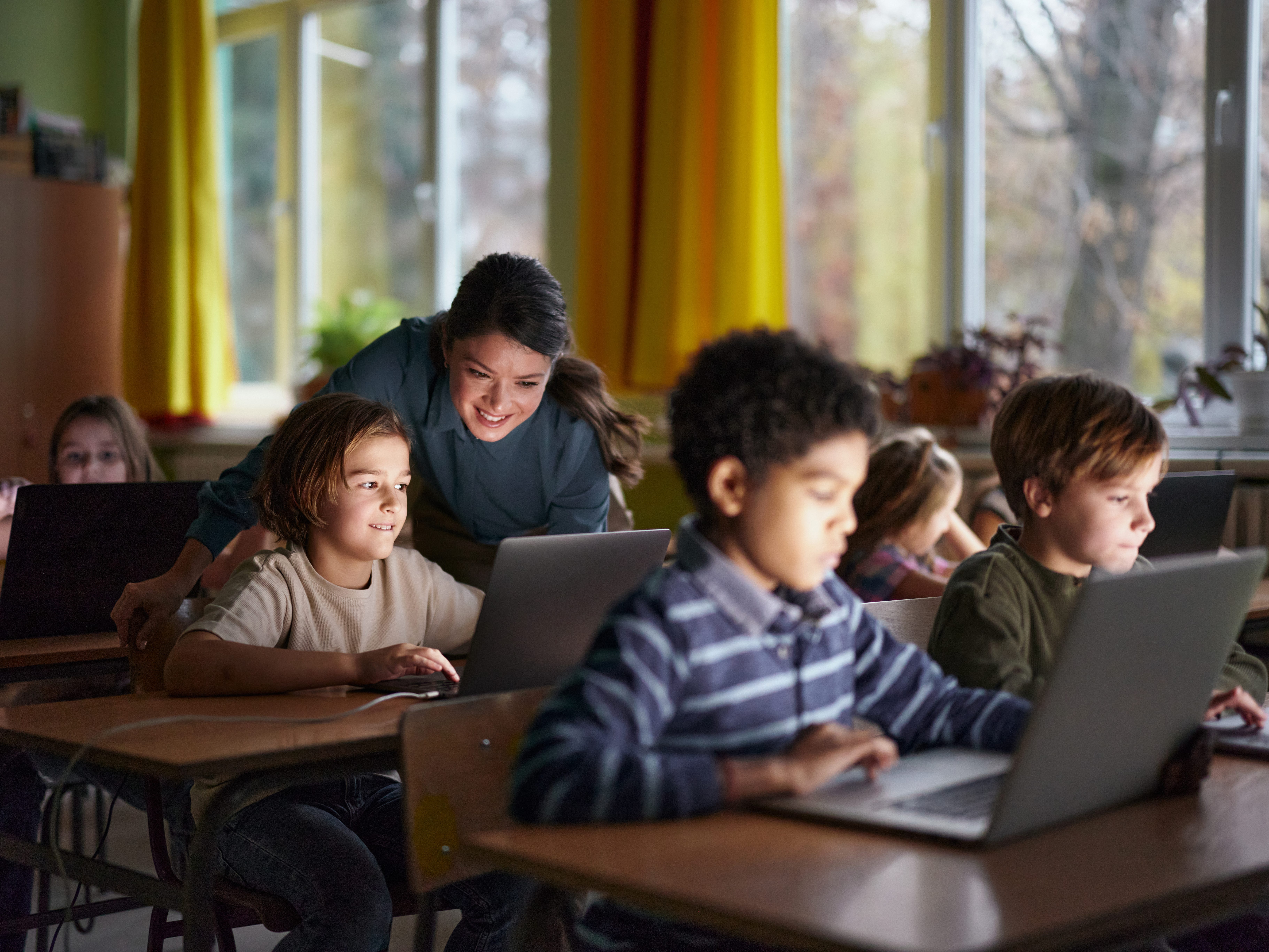 a teacher in a classroom with kids on laptops