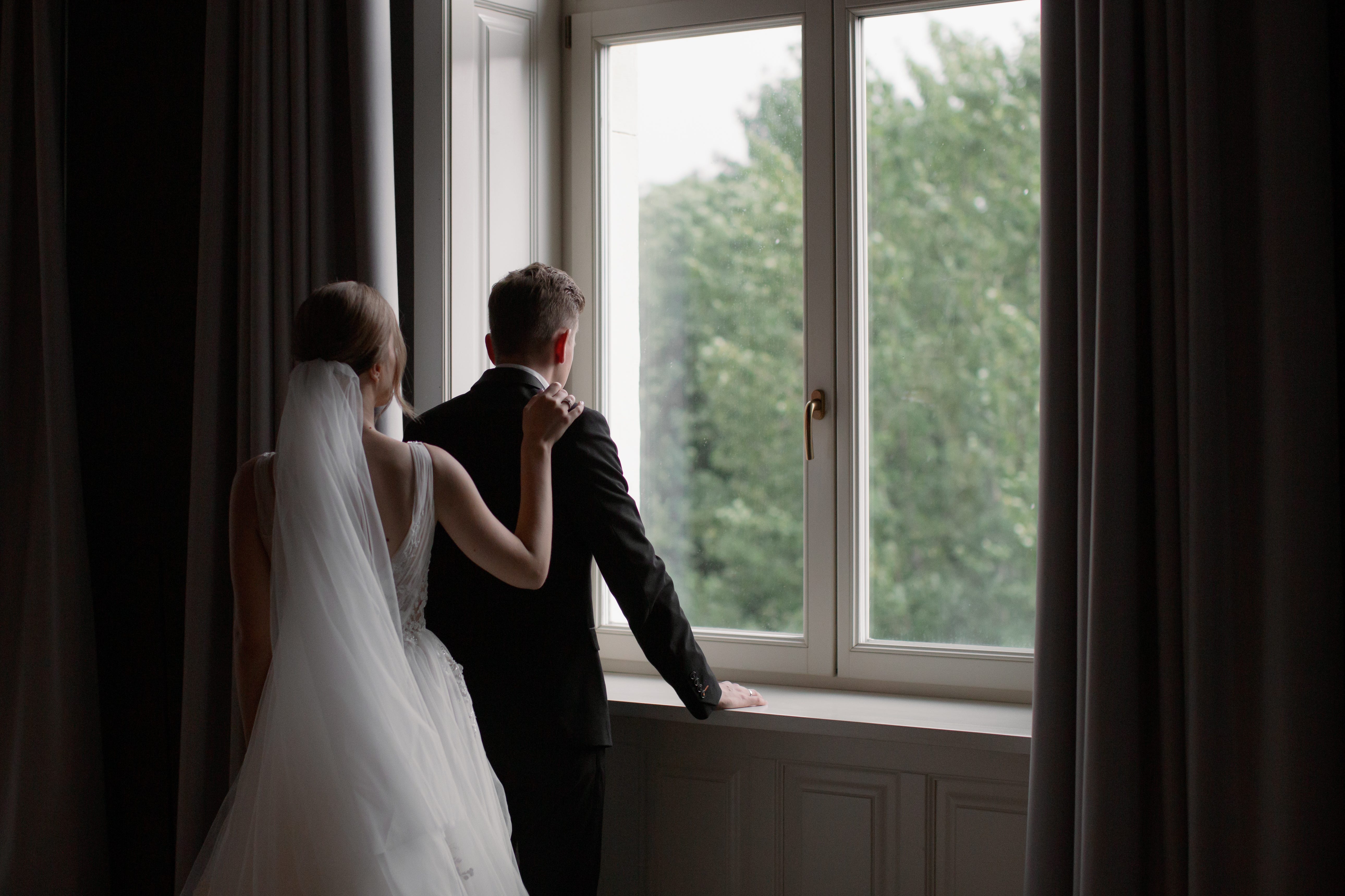A bride and groom look out the window.
