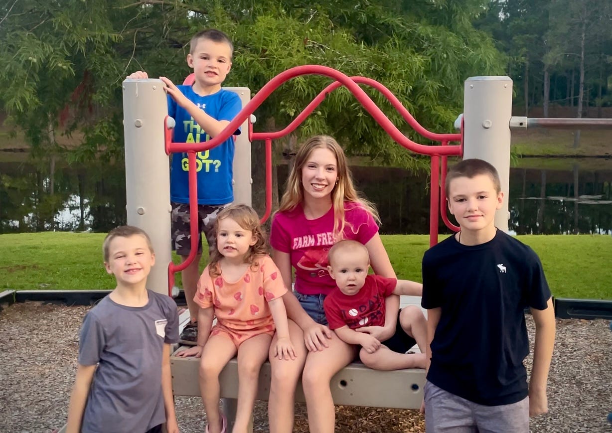 Six kids pose while on a piece of playground equipment at a park.