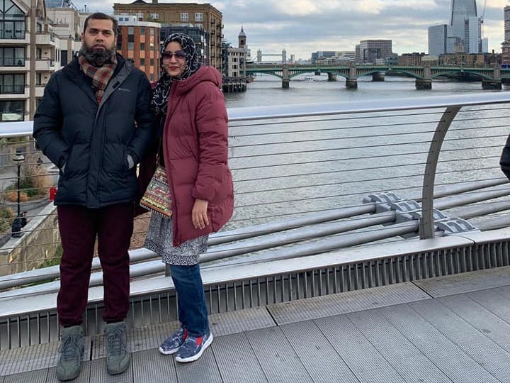 A couple stands on a bridge overlooking a city.