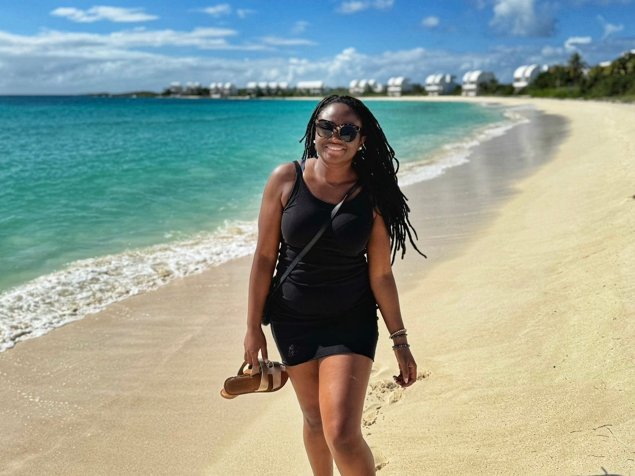 Mariette walking along a beach with sandals in her hand.