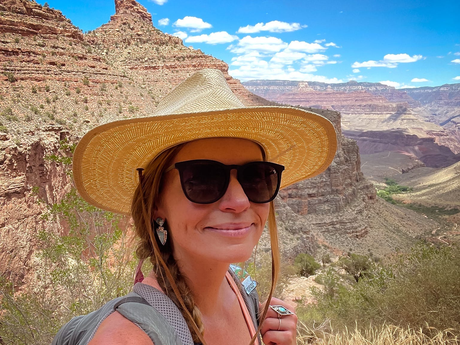 Emily takes a selfie wearing sunglasses and a beige hat, with the Grand Canyon behind her.