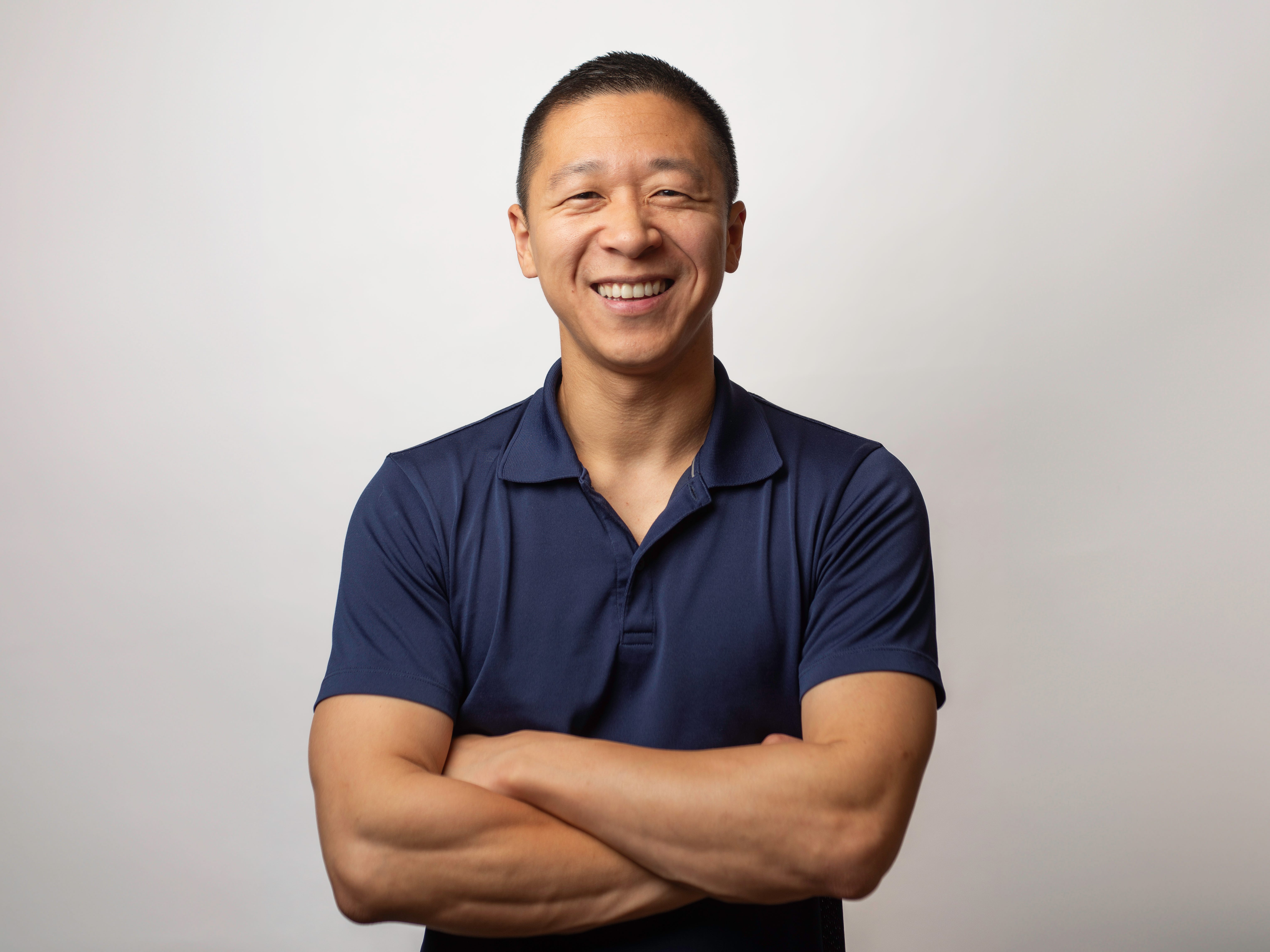 Sam Struan standing in front of a white background wearing a dark blue polo shirt with his arms folded.