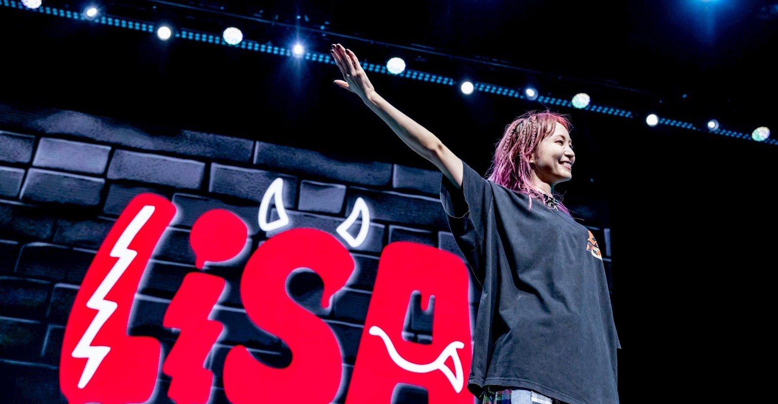 J-pop musician LiSA, on stage with a huge red sign featuring her name — with little devil horns on the “S” — in the background
