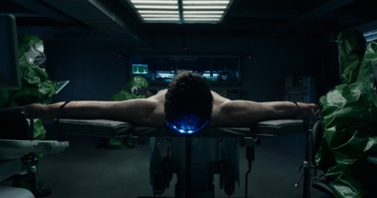Reed Richards, played by Miles Teller, is strapped to a table with his arms stretched in a scene from the 2015 Fantastic Four movie. 