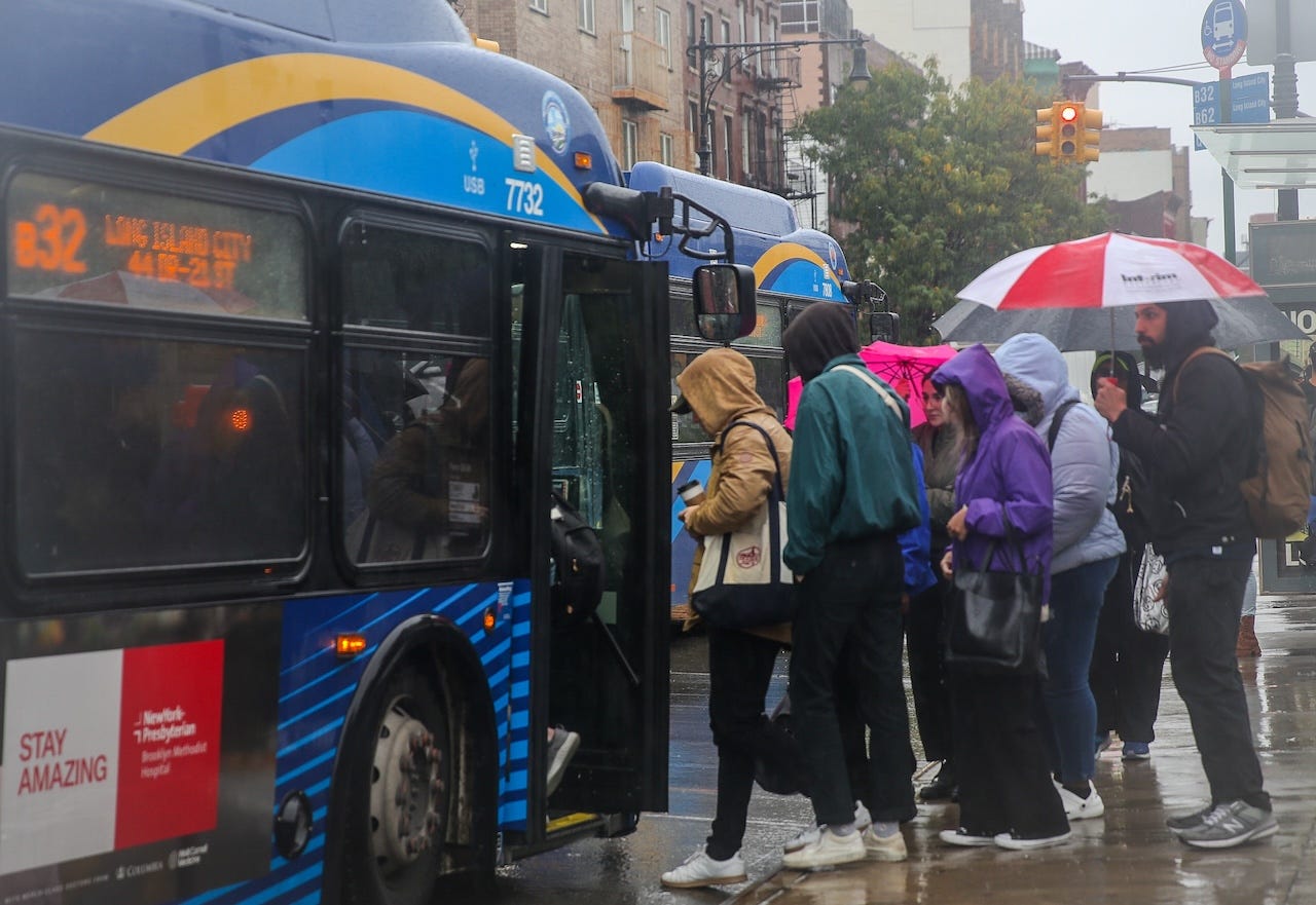 Passengers boarding a New York City public bus in heavy rain.