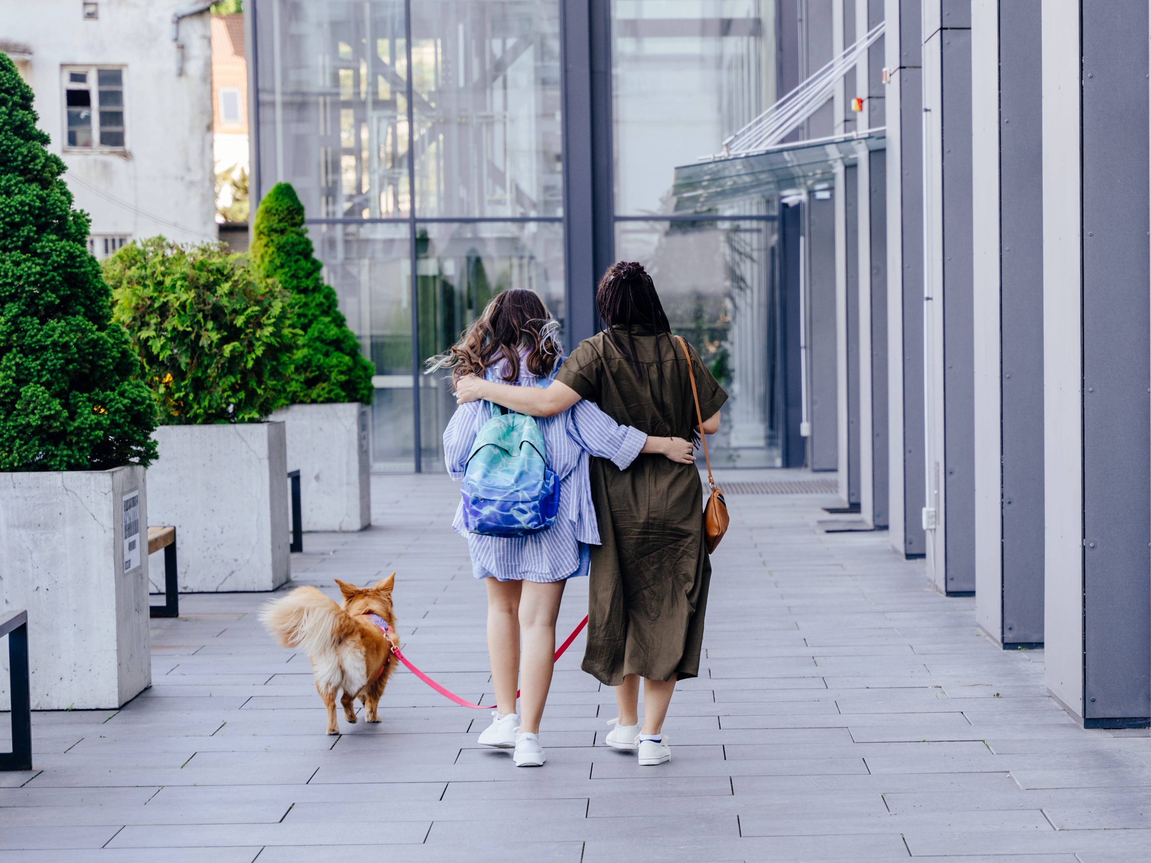 A mother and daughter walk arm-in-arm with a dog by their side.