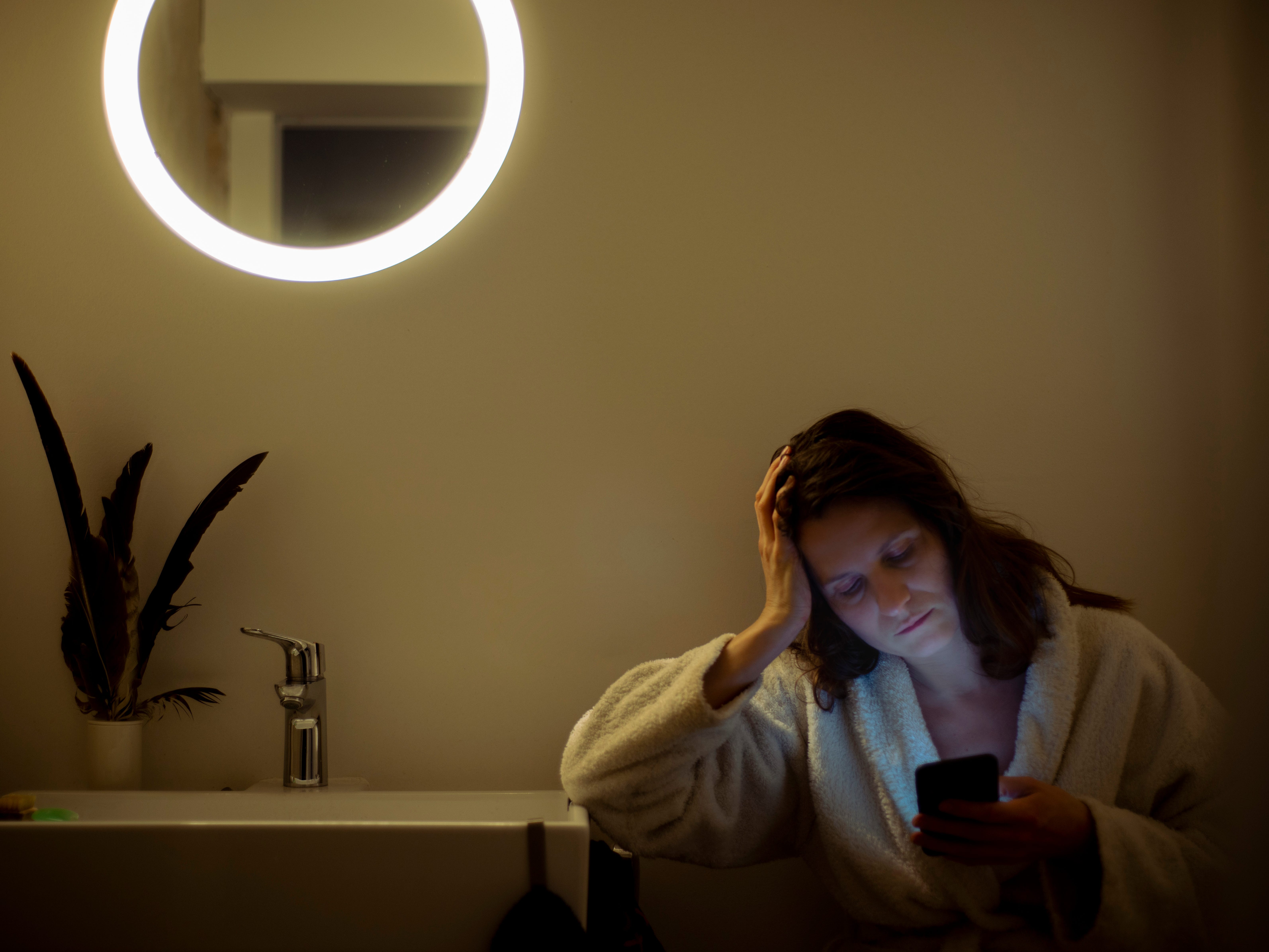 a woman sitting in the bathroom on her phone looking worried