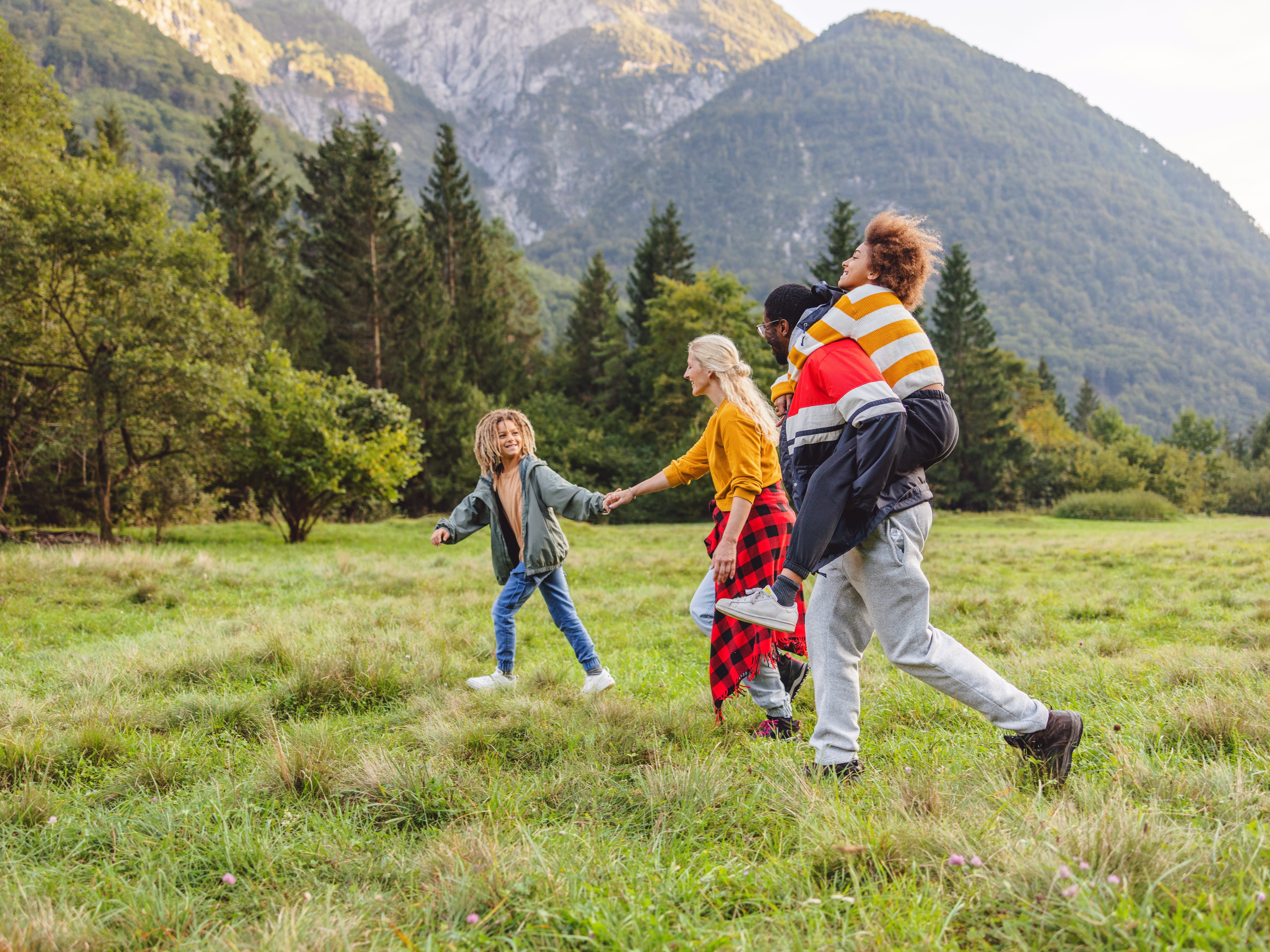 A family of four running in a field at the foot of a mountain.