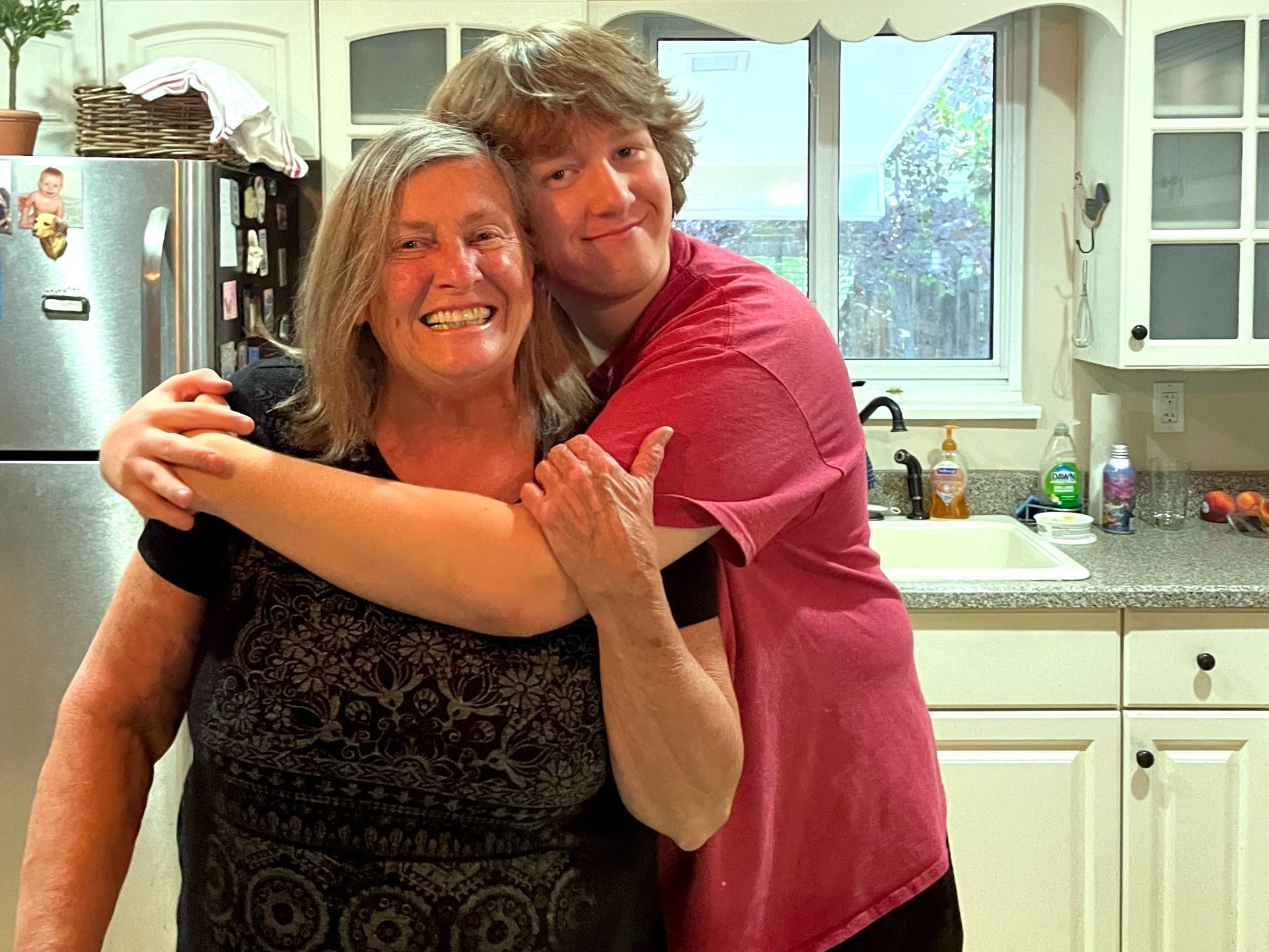 Teenage boy hugging older woman in kitchen