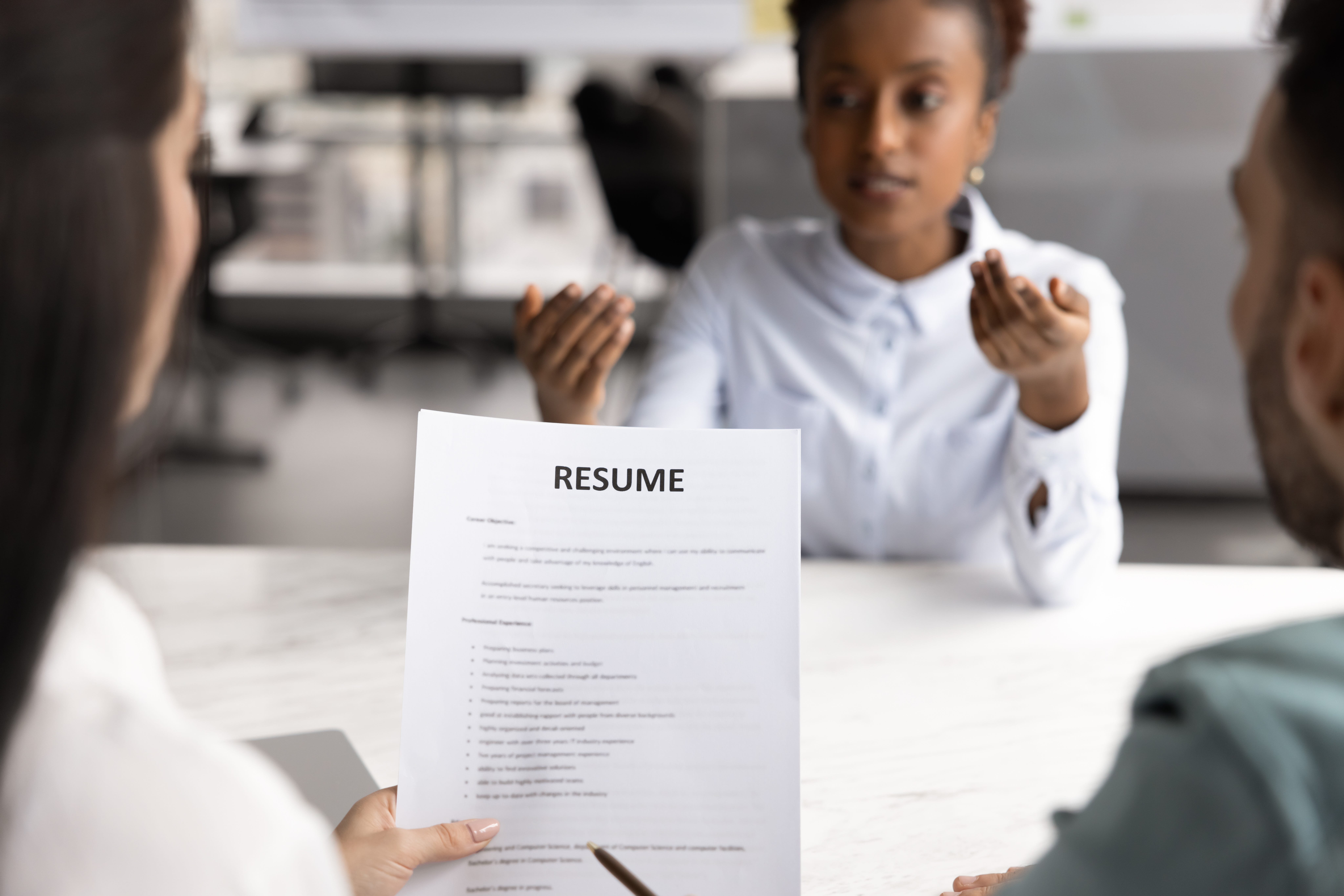 Company HR team interviewing African American job candidate woman, reviewing paper resume, talking to applicant about career, work experience, professional skills, achievement.