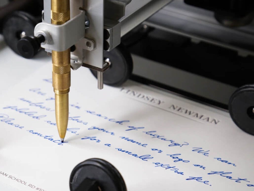A robotic arm holding a ballpoint pen writes a letter