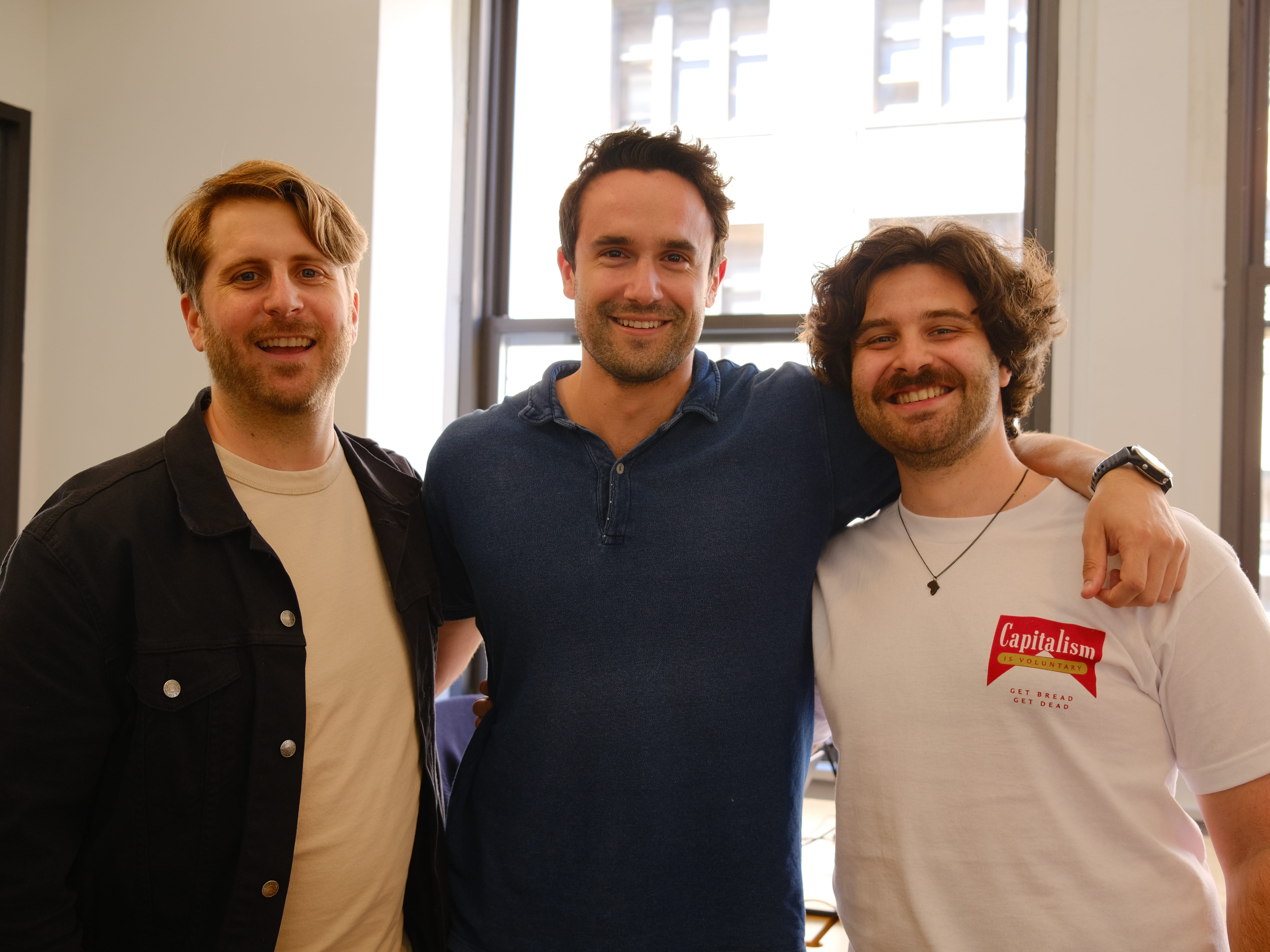 Cerebrium's Jono Irwin, Michael Louis, and Eli Roussos standing in front of windows, smiling with their arms around one another.