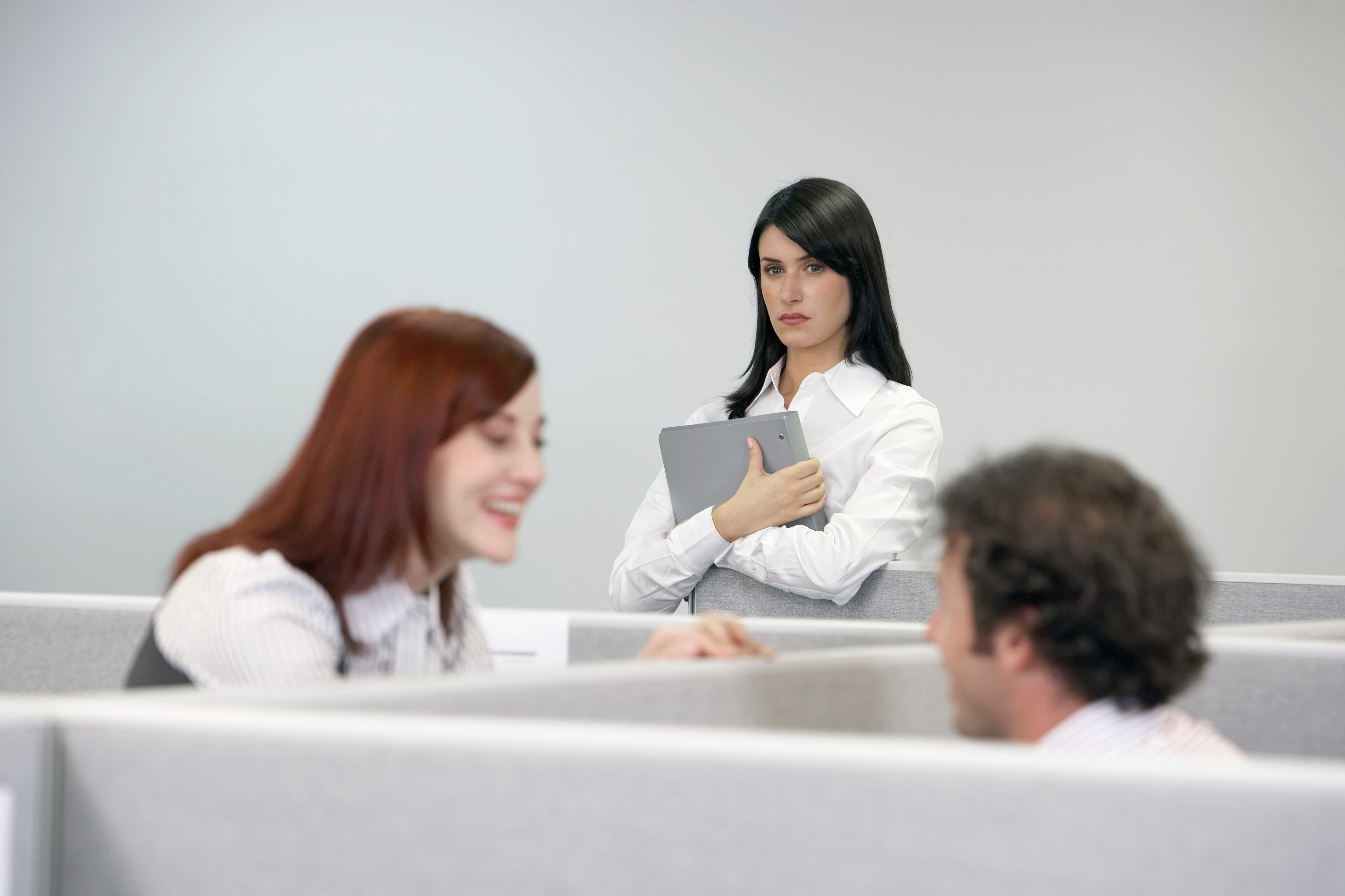 Businesswoman watching two coworkers talking over cubicle wall
