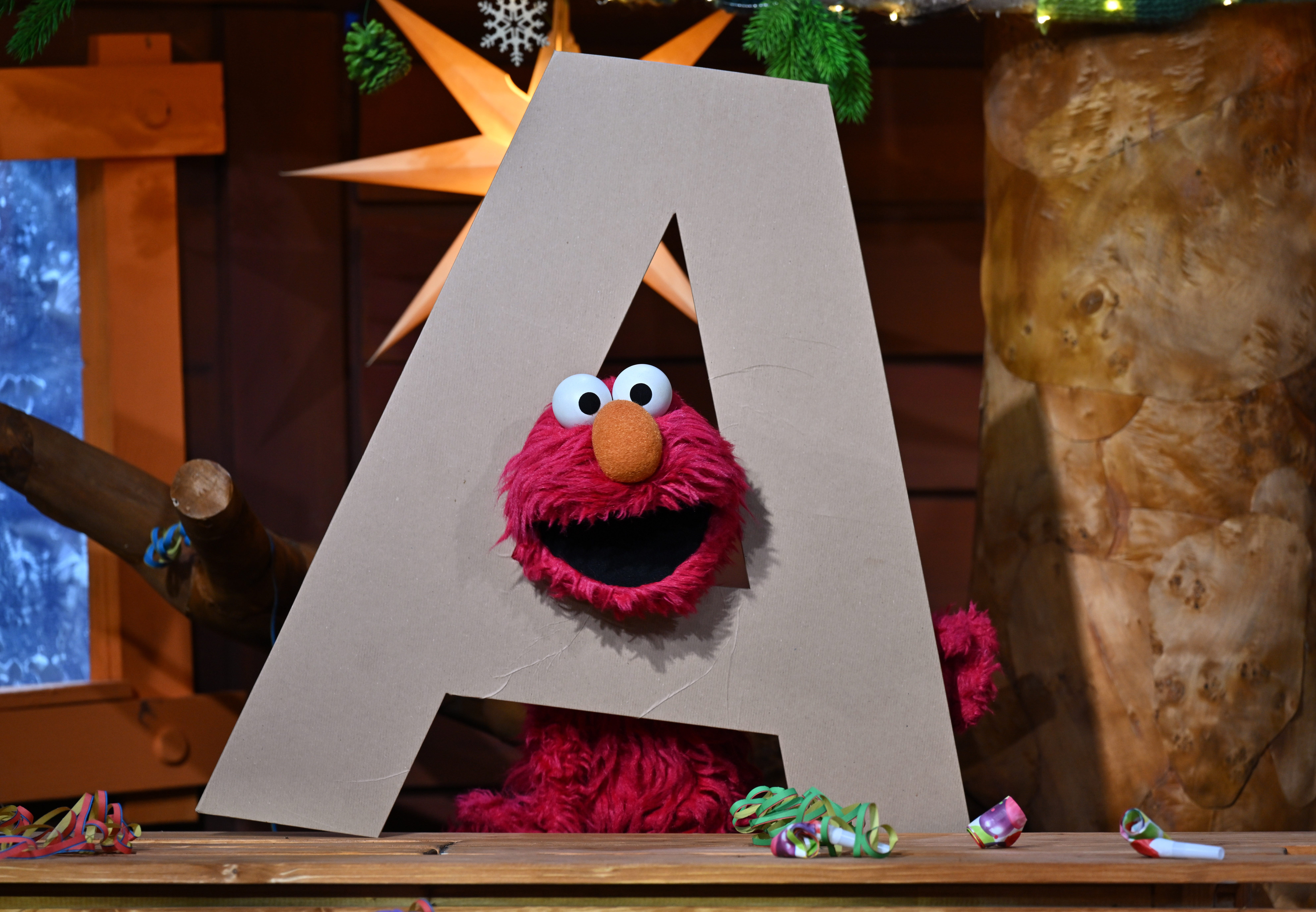 Elmo the Sesame Street with his head through a giant letter A