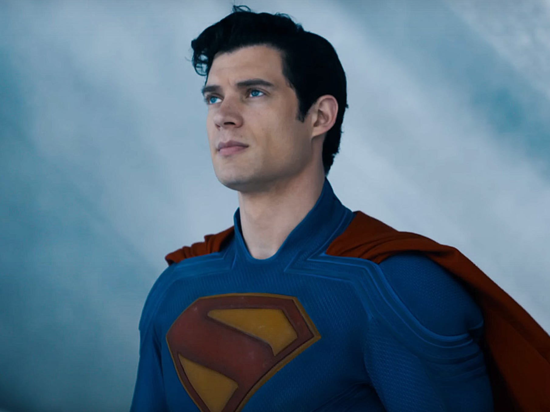 A man with slicked-back black hair is standing in an icy location. He's wearing a blue superhero costume. On his chest, there is a yellow and red diamond 'S' symbol. He is also wearing a red cape.