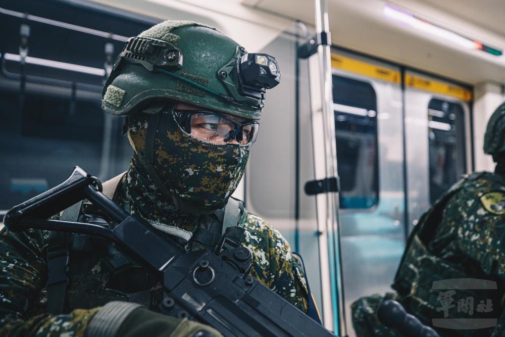 A Taiwanese soldier with military headgear, a balaclava, and eyeglasses holds a firearm in a subway car.