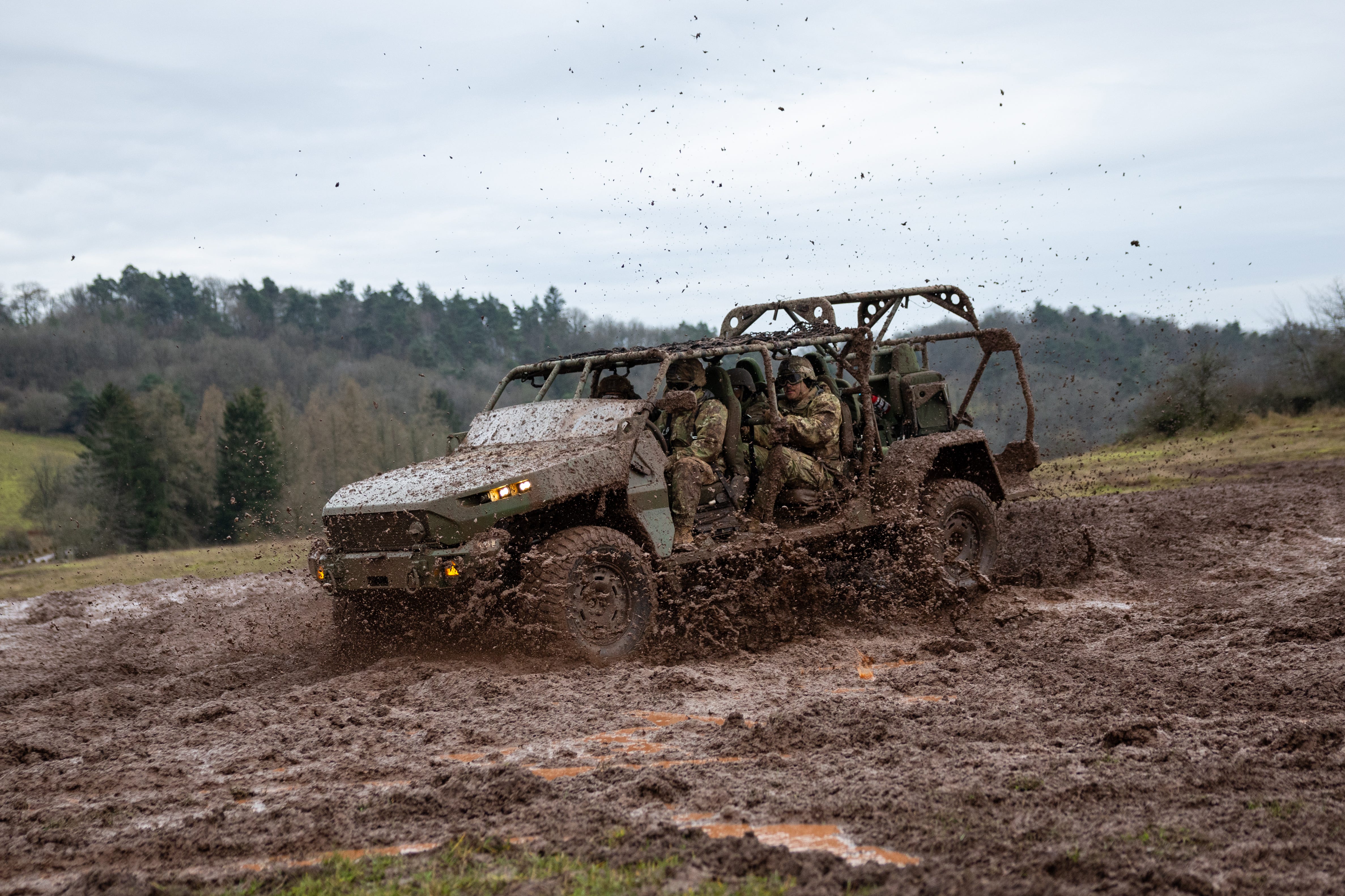 An infantry squad vehicle driving in mud with a forest and overcast sky in the background.