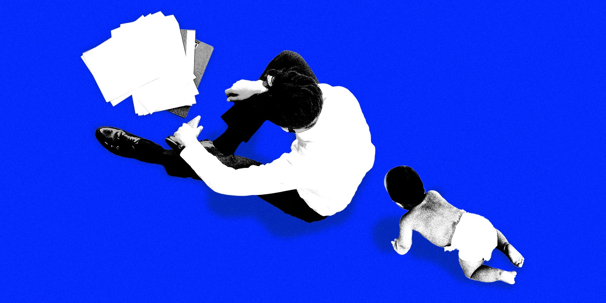 A father sitting in front of paper work while his child crawls towards him from behind