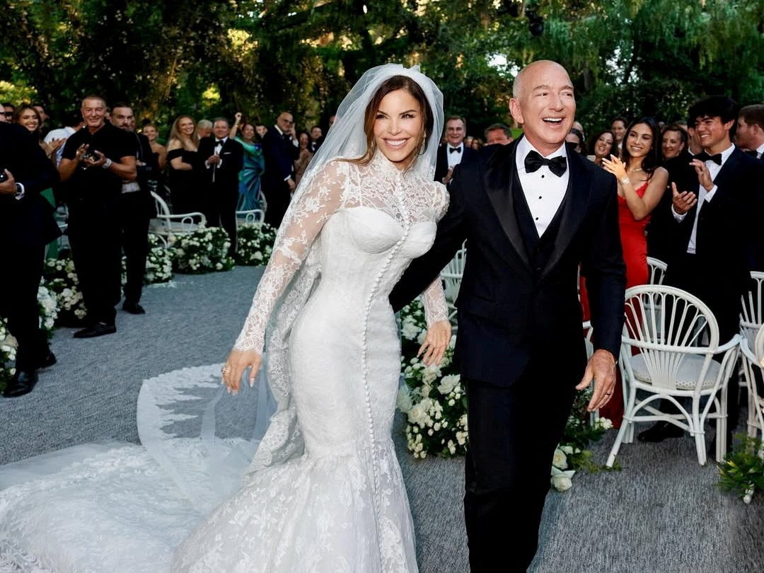 Lauren Sánchez, dressed in a white gown and veil, and Jeff Bezos, wearing a black tuxedo, walk down the aisle after the Venice wedding ceremony.